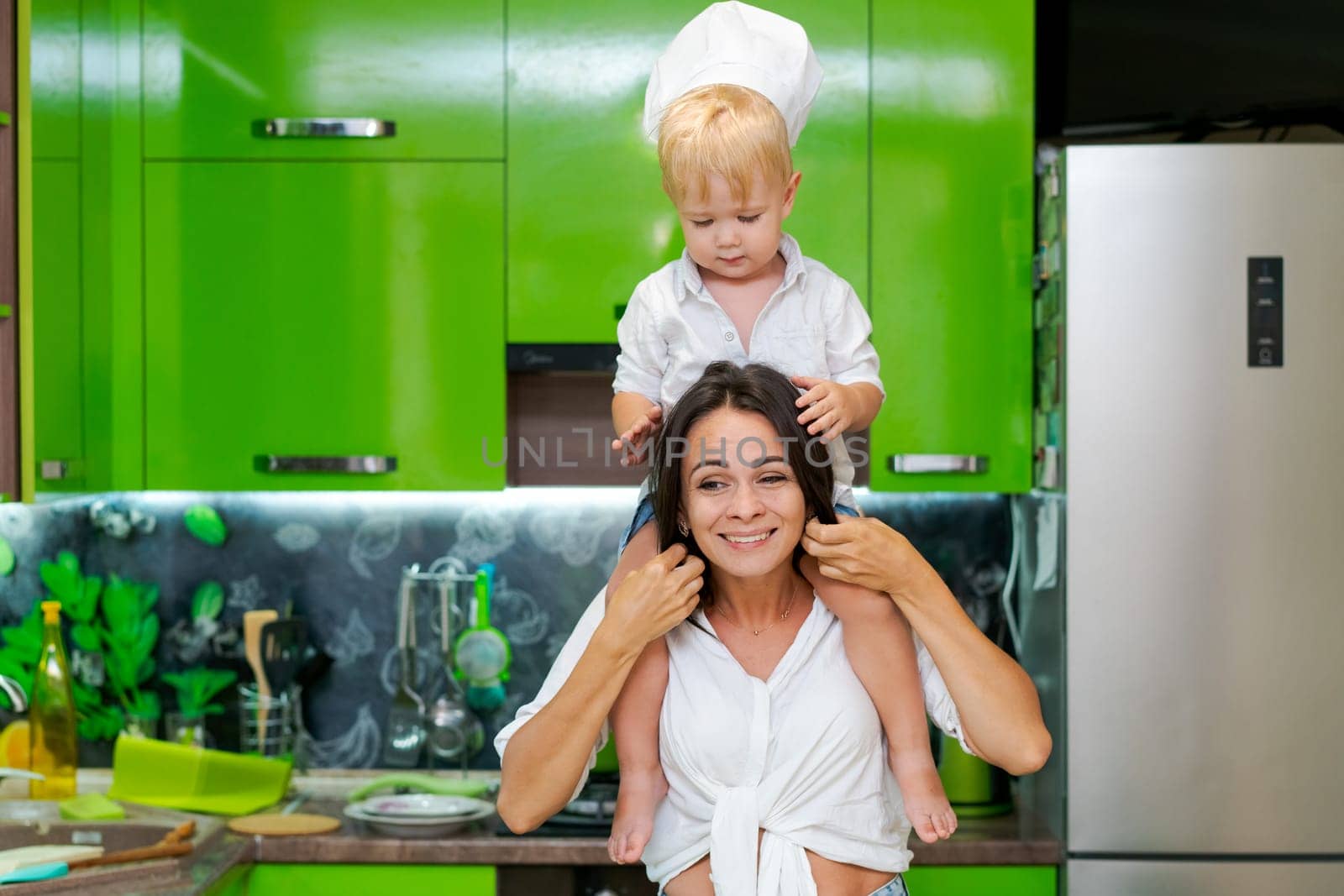 happy family, mother holding her son in her arms in the kitchen by EkaterinaPereslavtseva