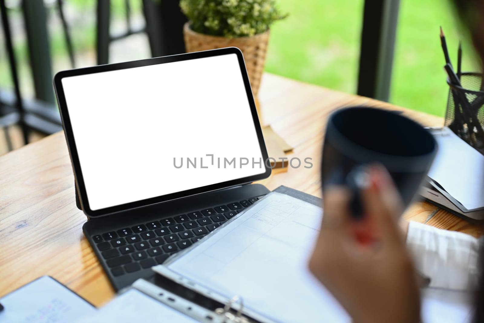 Cropped shot of businesswoman holding coffee cup and using digital tablet on wooden office desk.