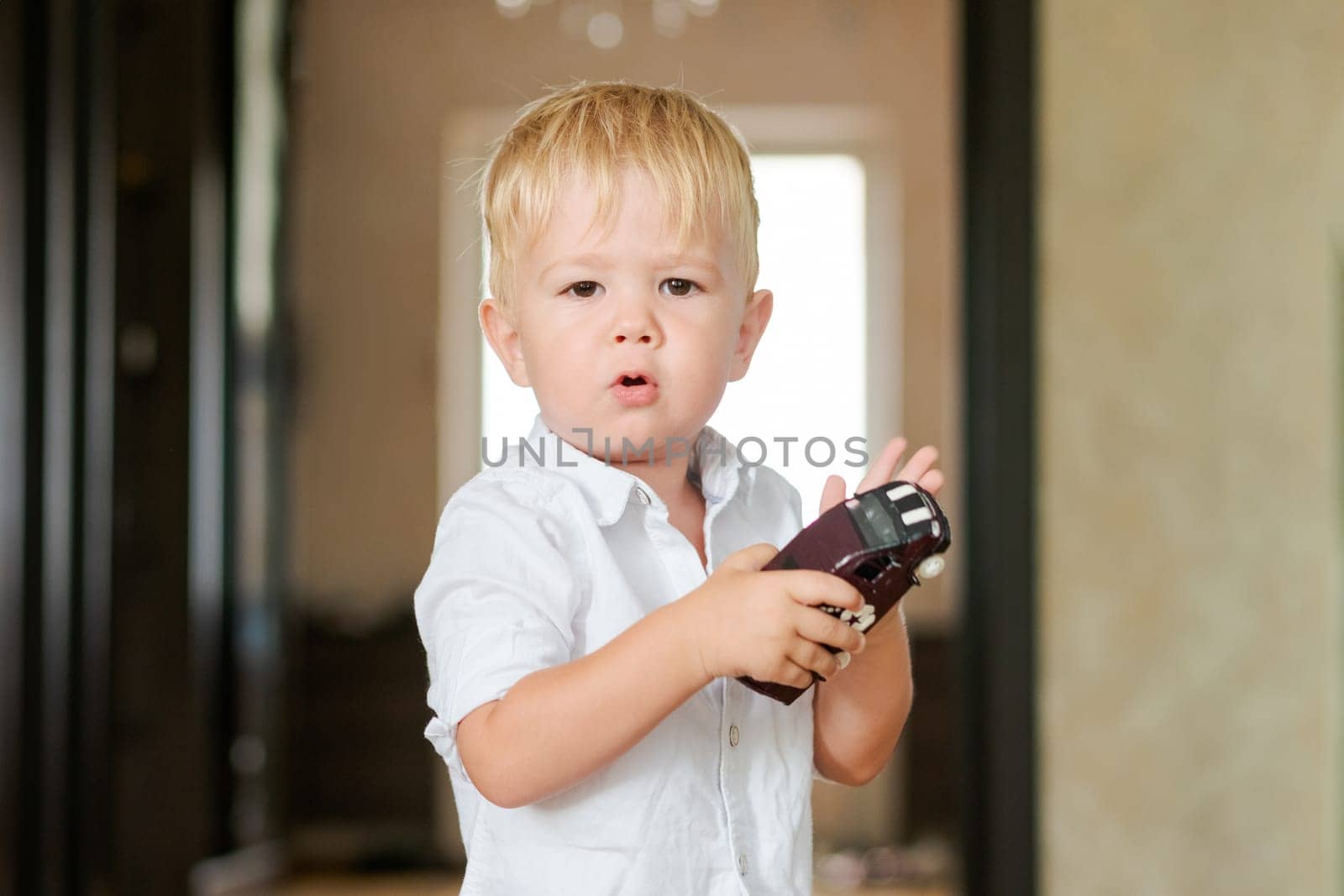 a little boy stands in the room and holds a toy car in his hands