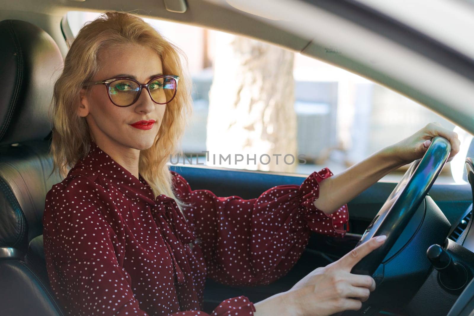 beautiful successful blonde woman in a red dress sitting in a car behind the wheel