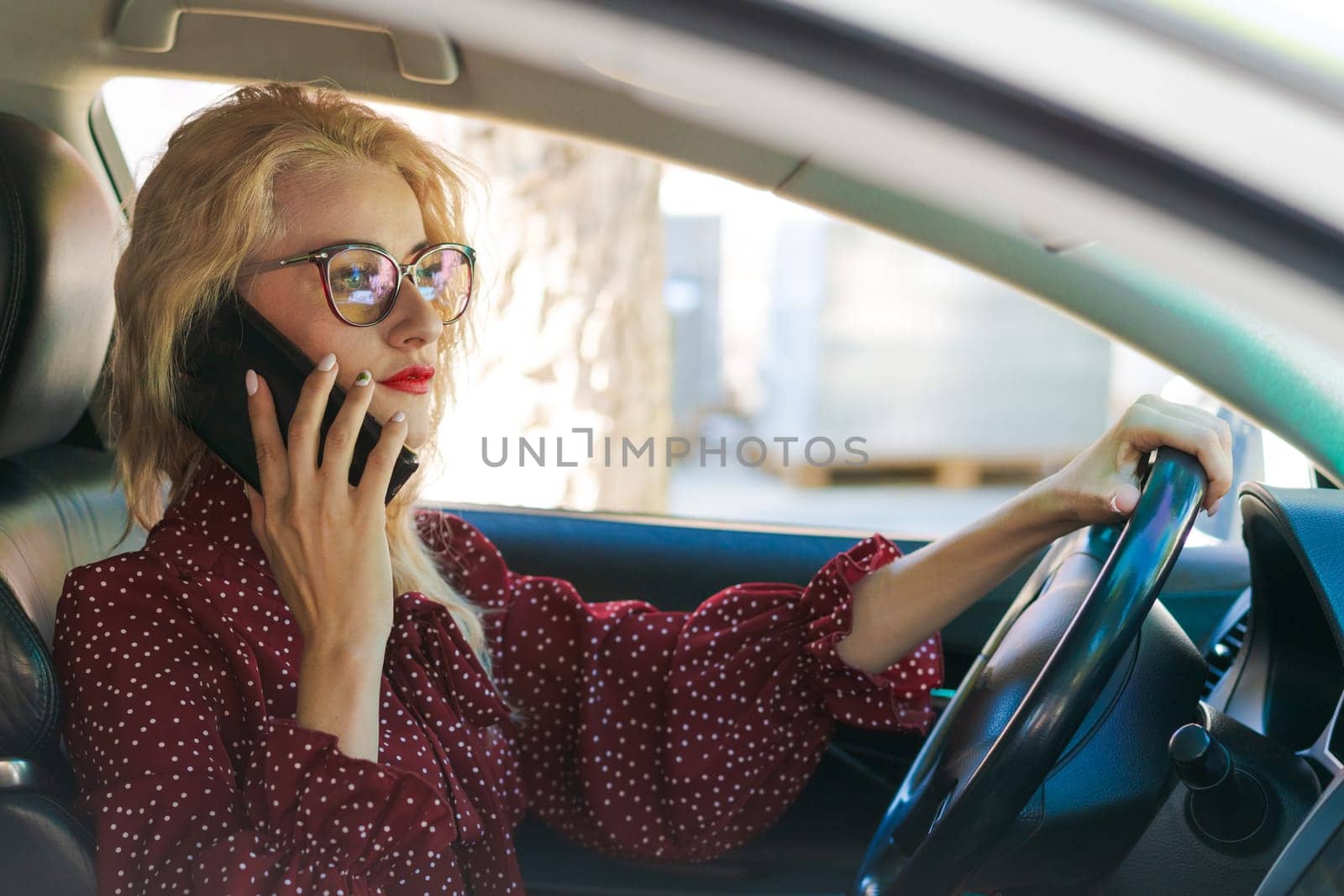 portrait of a beautiful blonde woman in a red dress sitting in a car with a phone