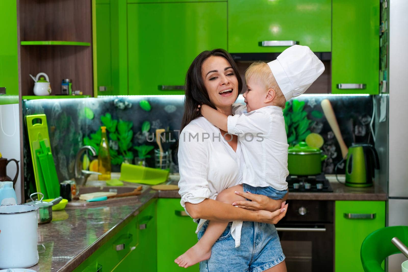 happy family, mother holding her son in her arms in the kitchen by EkaterinaPereslavtseva