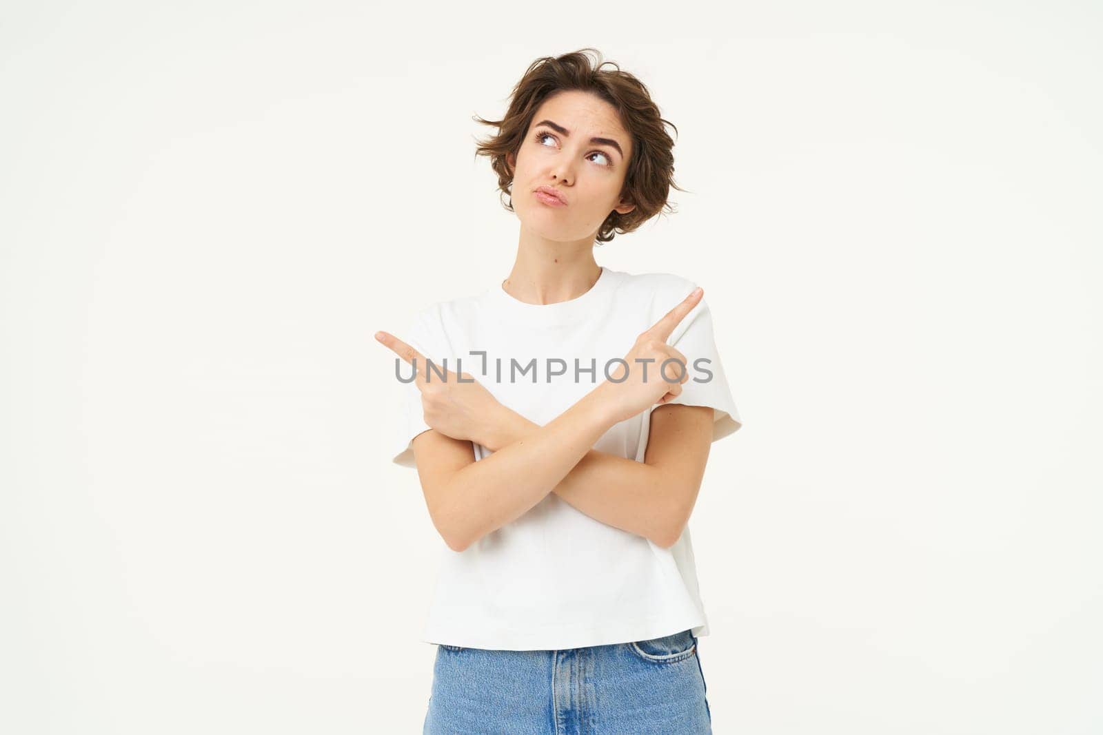 Portrait of brunette woman with thoughtful face, pointing sideways, making choice, decision, standing over white studio background by Benzoix