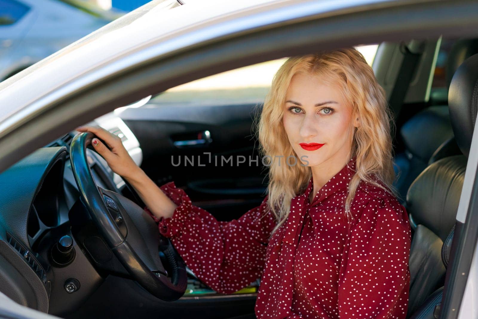 beautiful successful blonde woman in a red dress sitting in a car behind the wheel