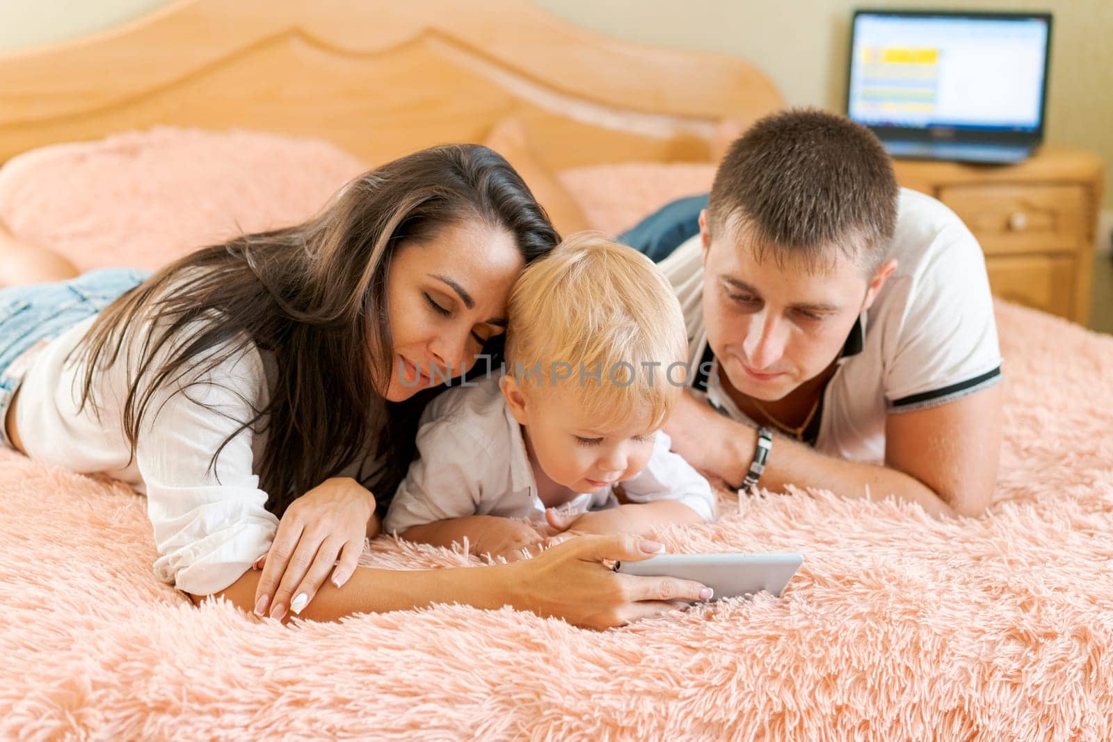 happy family lying on the bed looking at the phone, mom dad and little son