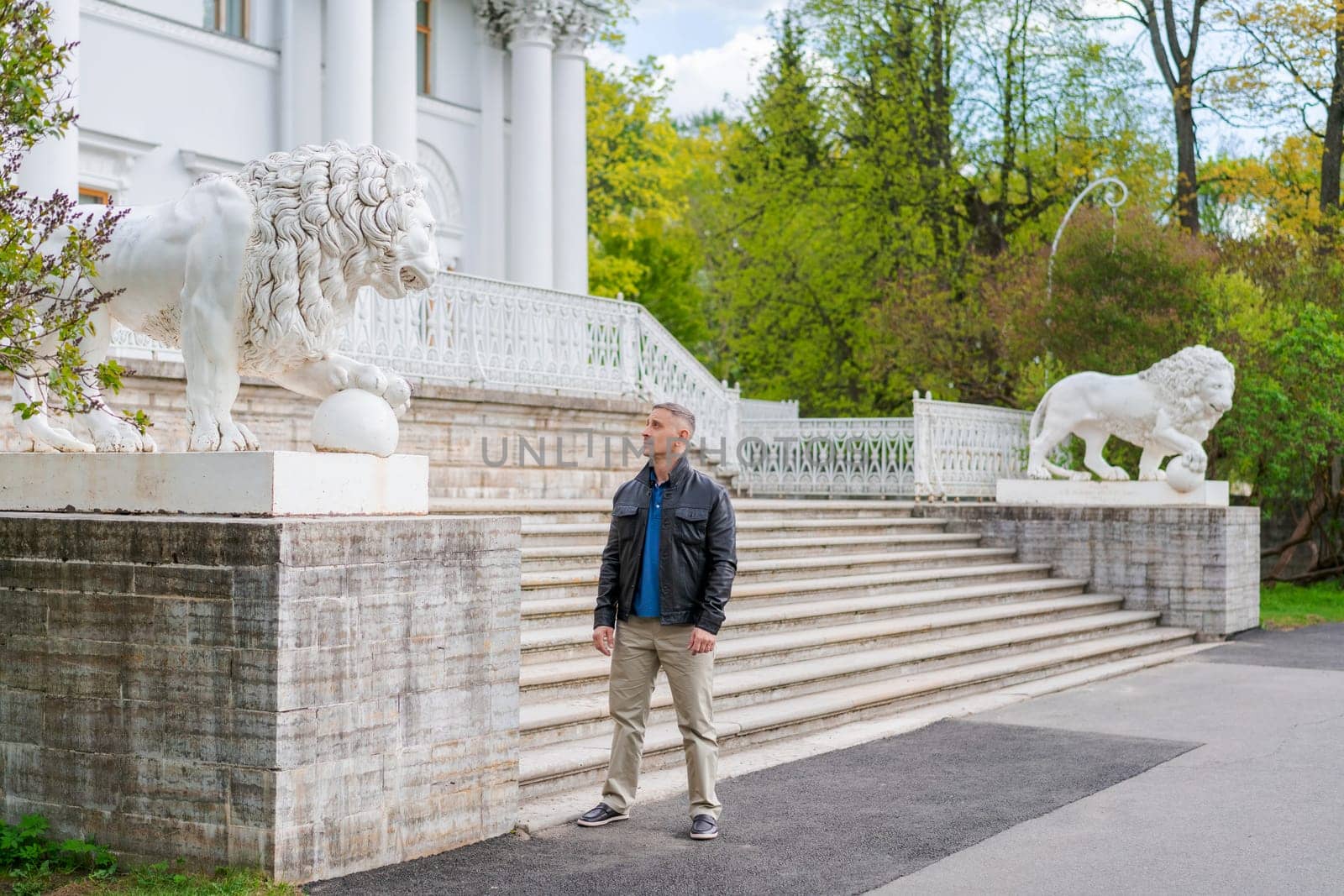 a man in casual clothes stands near a beautiful white building with lions by EkaterinaPereslavtseva