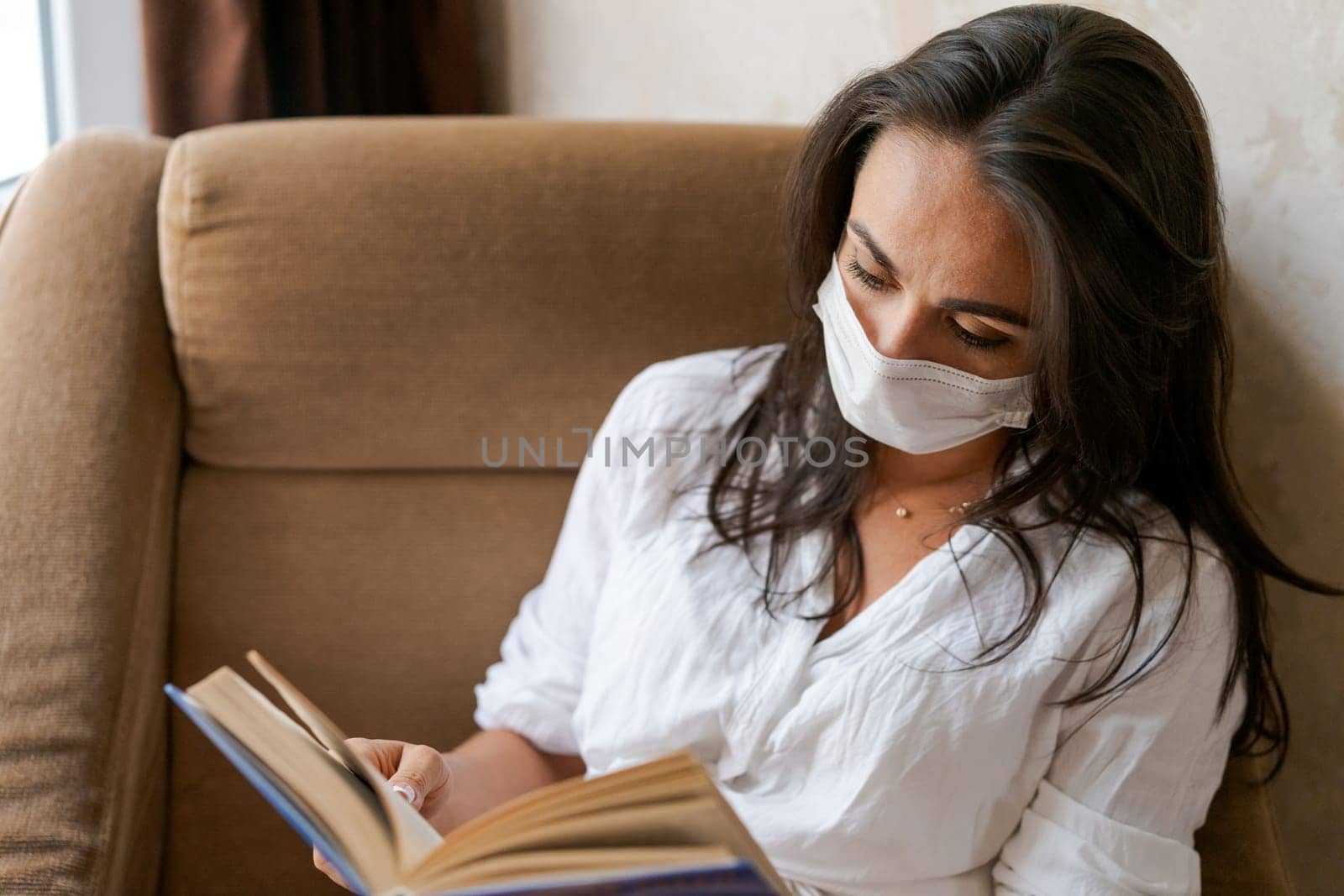 woman sitting on a chair with a protective mask holds a book in her hand, lifestyle concept