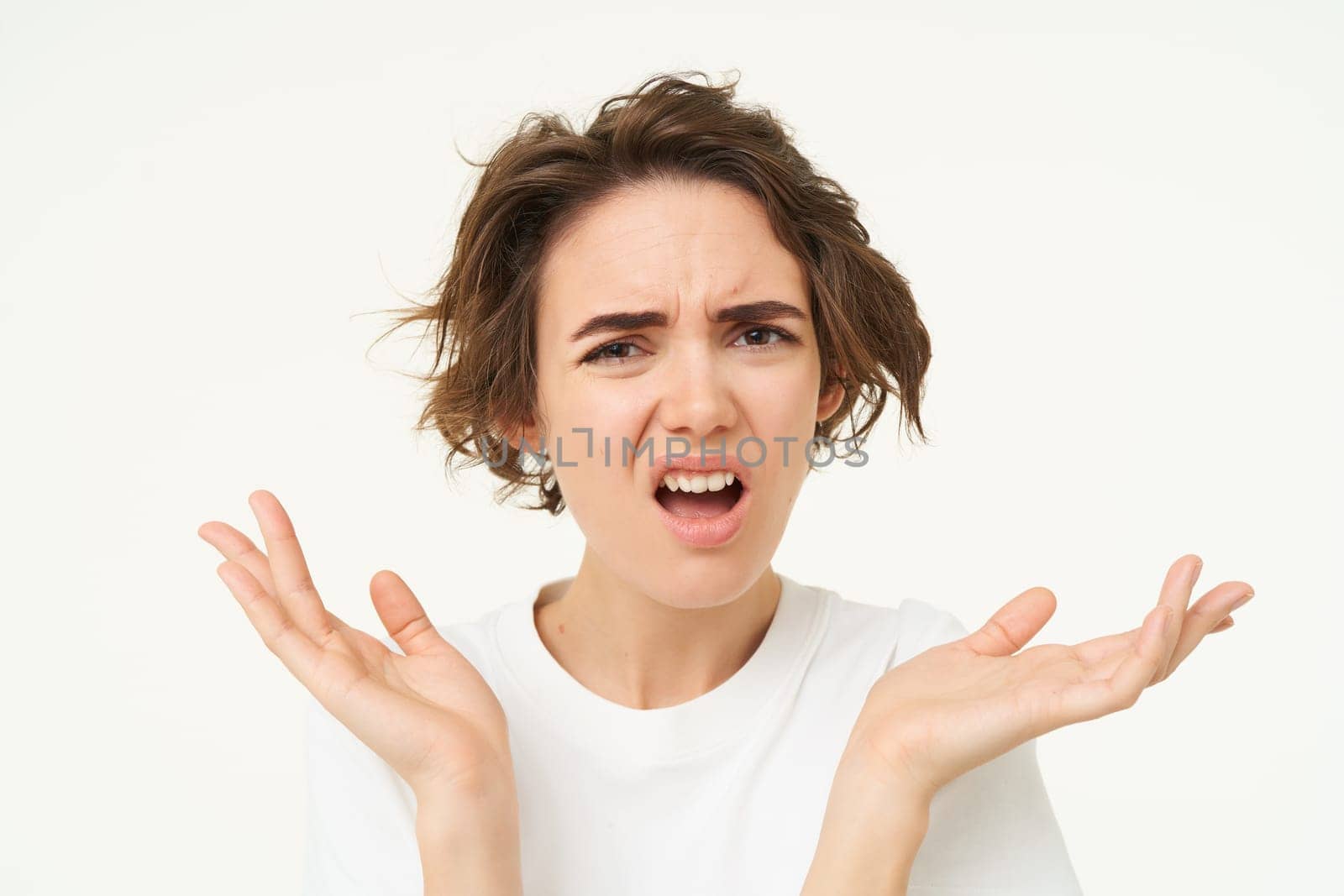 Close up of shocked brunette woman, shrugging and looking disappointed, posing over white studio background.