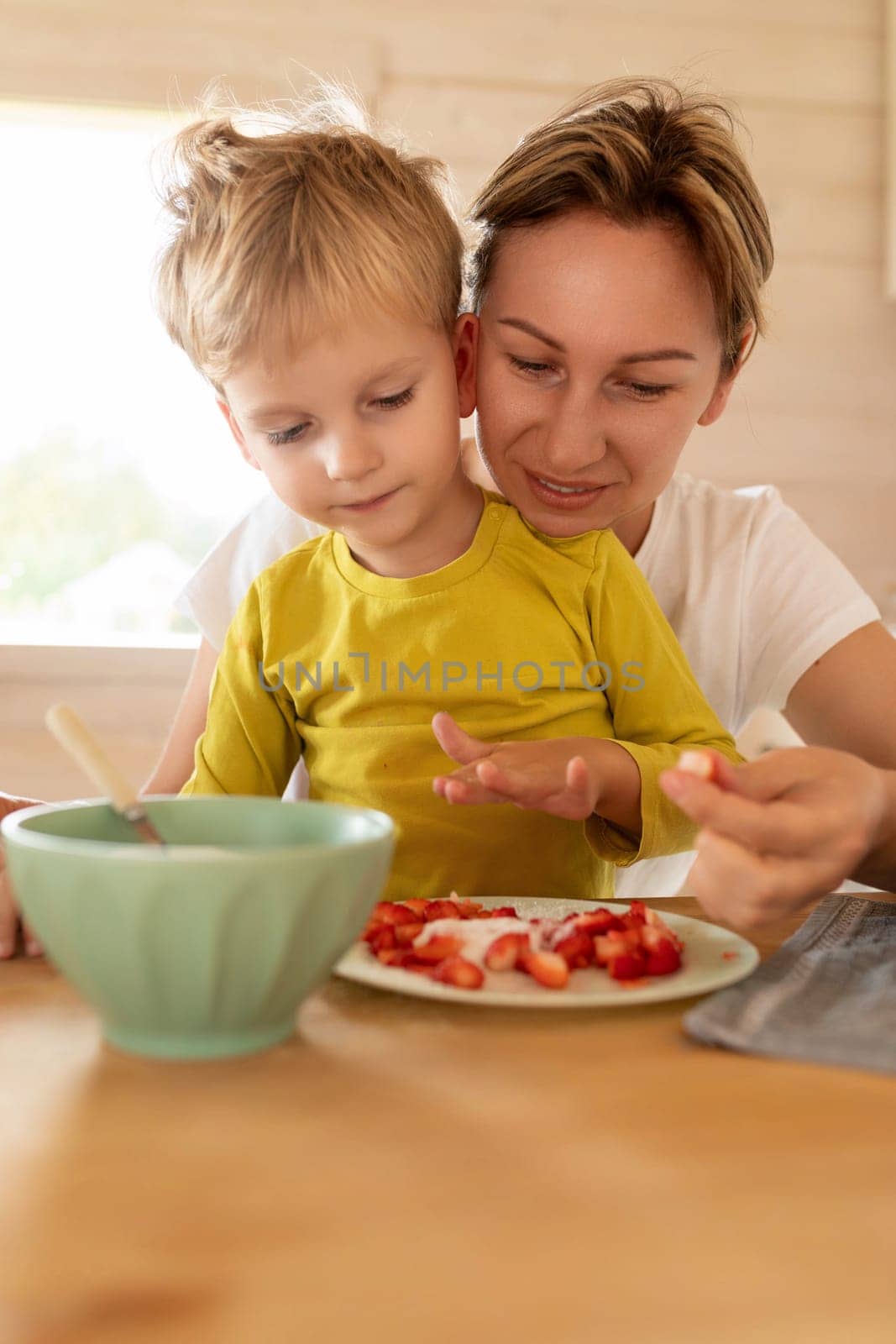 little Caucasian blond son and mother having breakfast with delicious food.