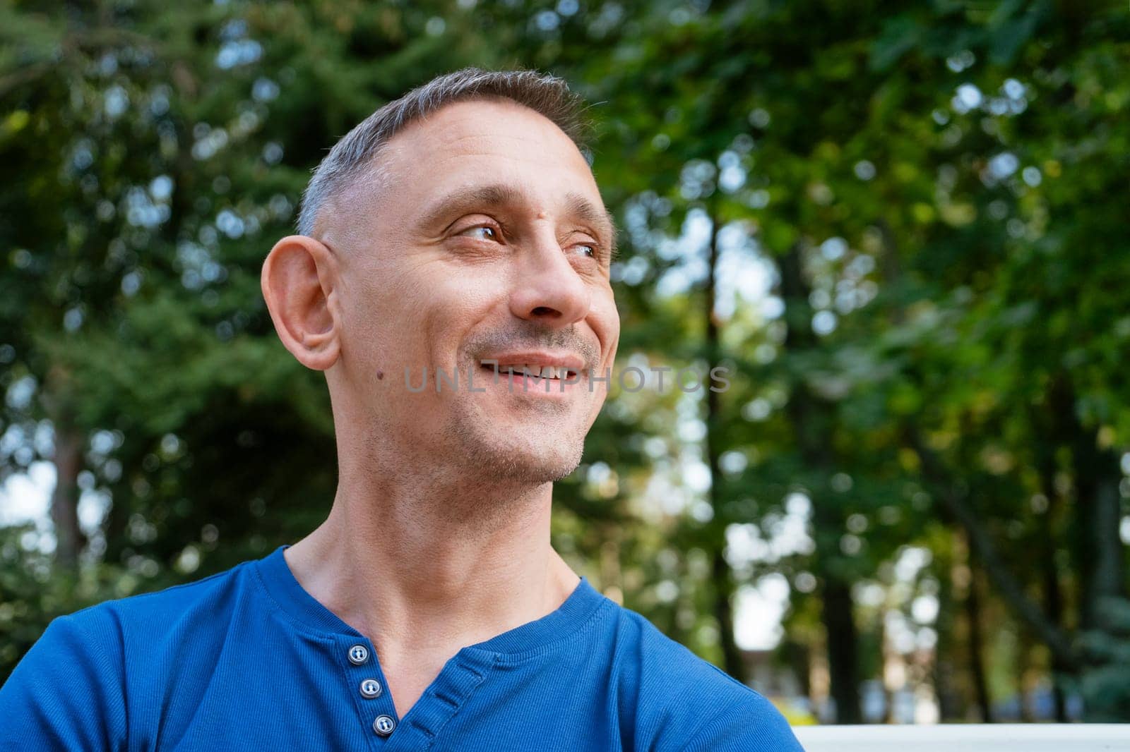 handsome portrait of a man in a blue T-shirt sitting on a park bench