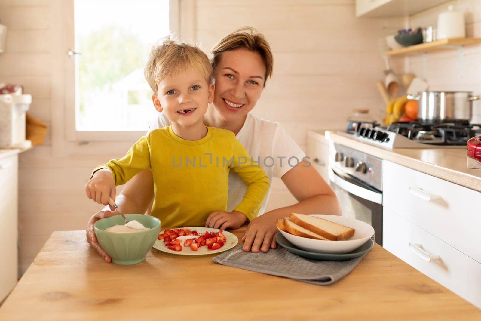 cheerful Caucasian mother and little son are sitting in the kitchen and preparing breakfast by TRMK