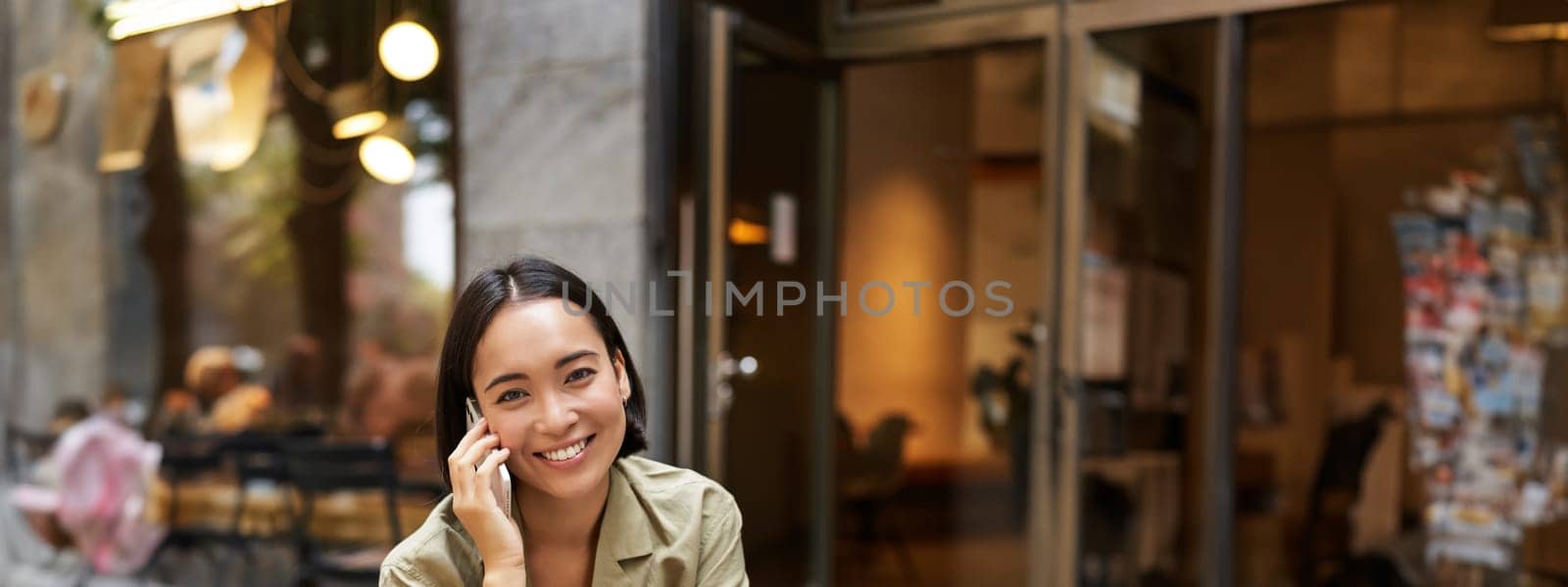 Happy girl calling on mobile phone, talking on smartphone and working with laptop, doing homework, studying outdoors from cafe by Benzoix