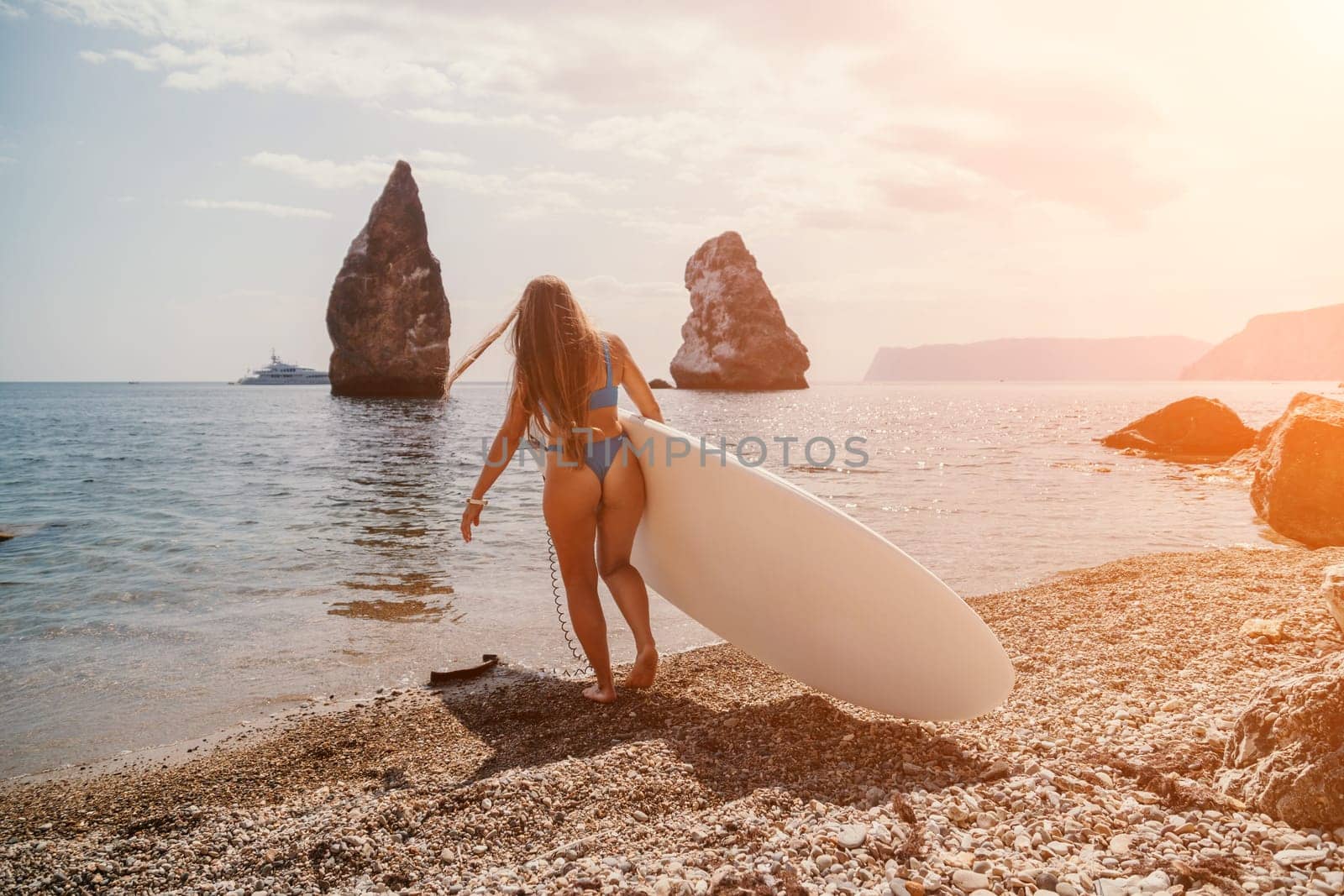 Close up shot of beautiful young caucasian woman with black hair and freckles looking at camera and smiling. Cute woman portrait in a pink bikini posing on a volcanic rock high above the sea