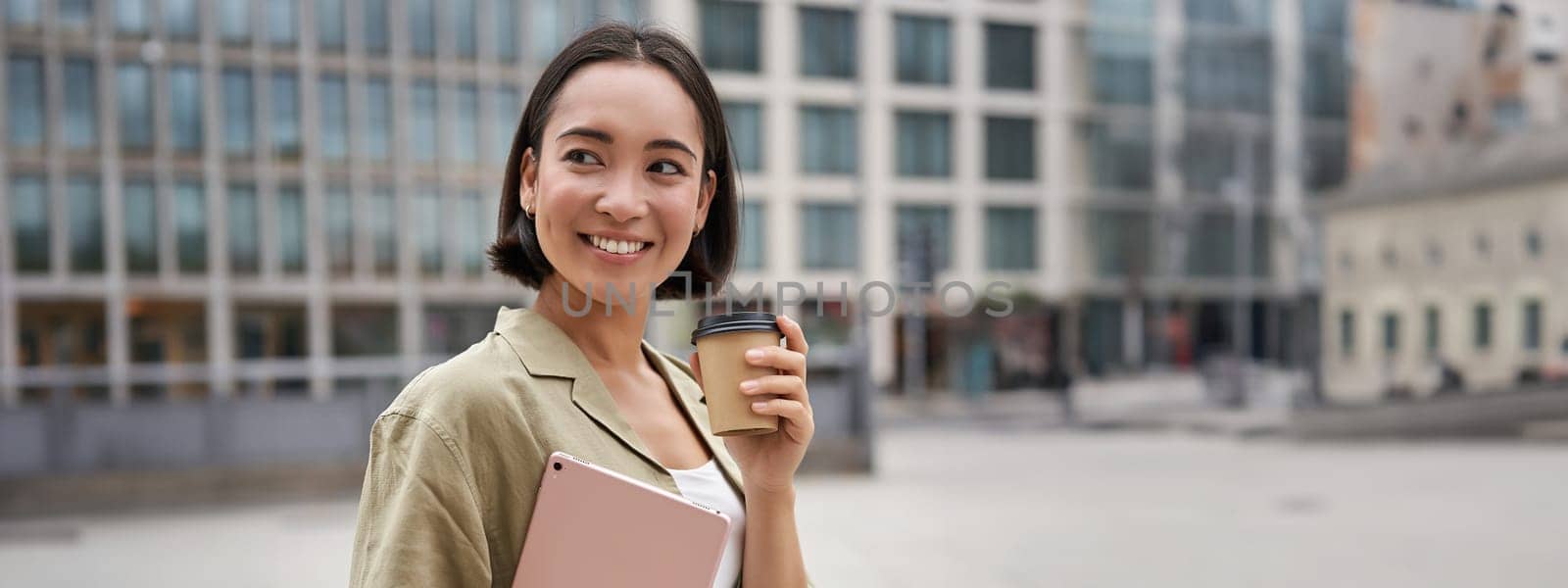 Portrait of asian girl with tablet, drinks coffee on street, walking in city centre by Benzoix