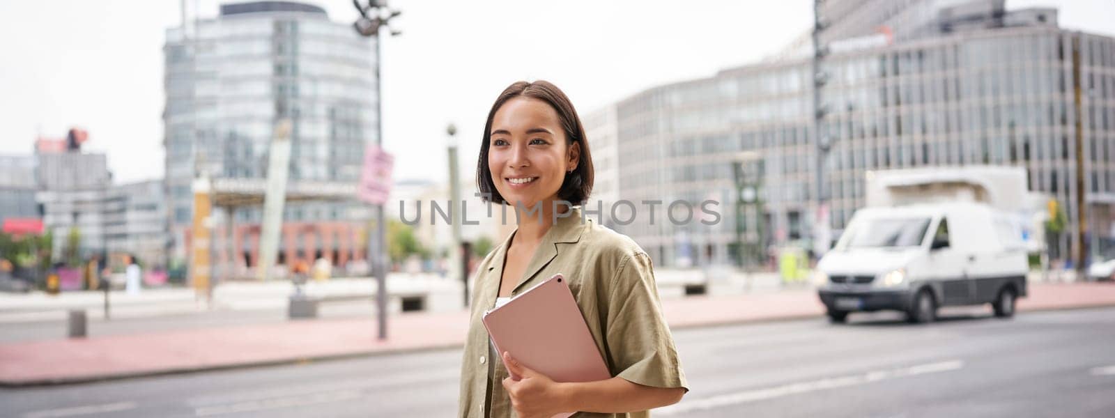 Portrait of young stylish woman walking with tablet, going somewhere in city by Benzoix