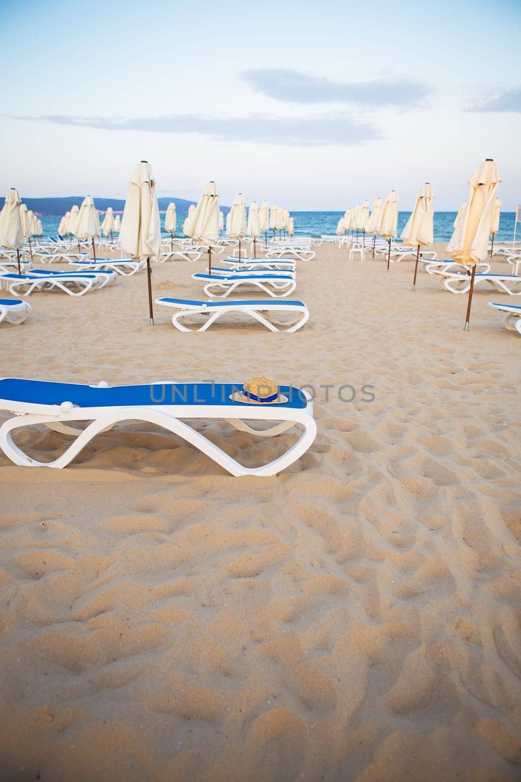 a straw hat rests on a deck-chair near the sea.