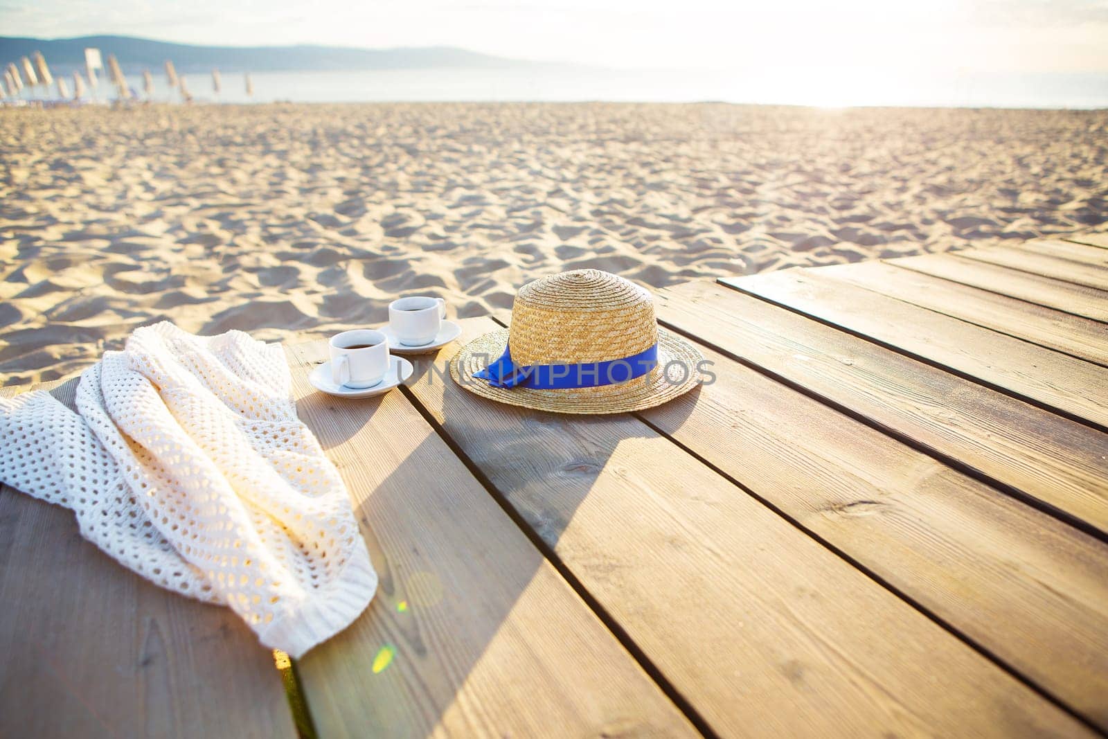 a hat, a cape and two cups of coffee stand on a pier near the sea.