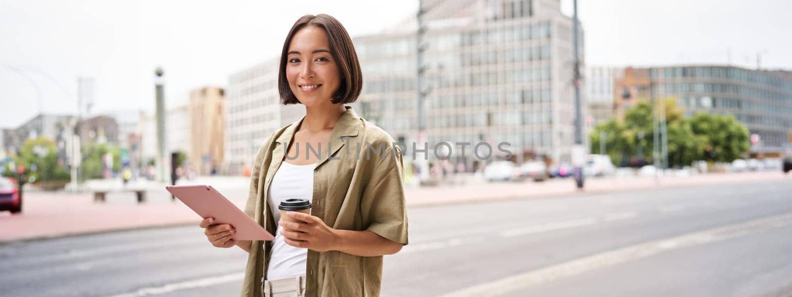 Portrait of asian girl standing on street with tablet, drinking coffee.