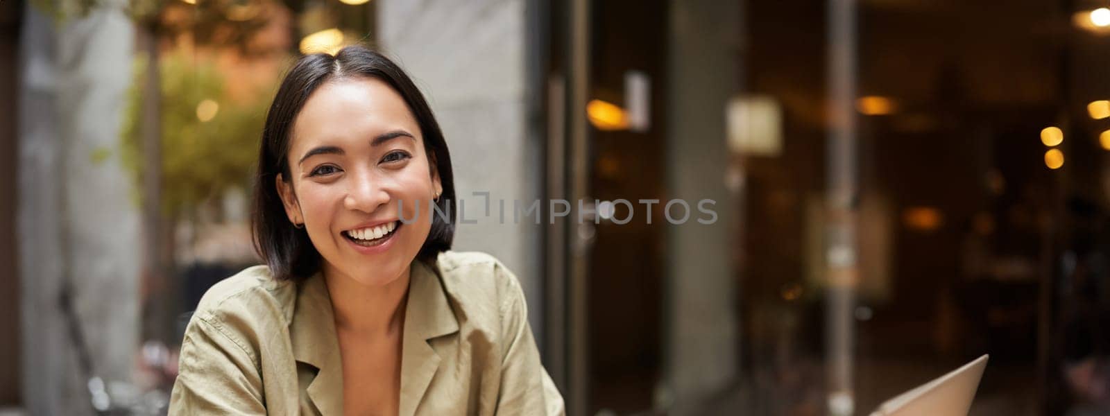 Smiling young woman working from cafe or co-working space, sitting with laptop, studying or doing homework, looking happy by Benzoix