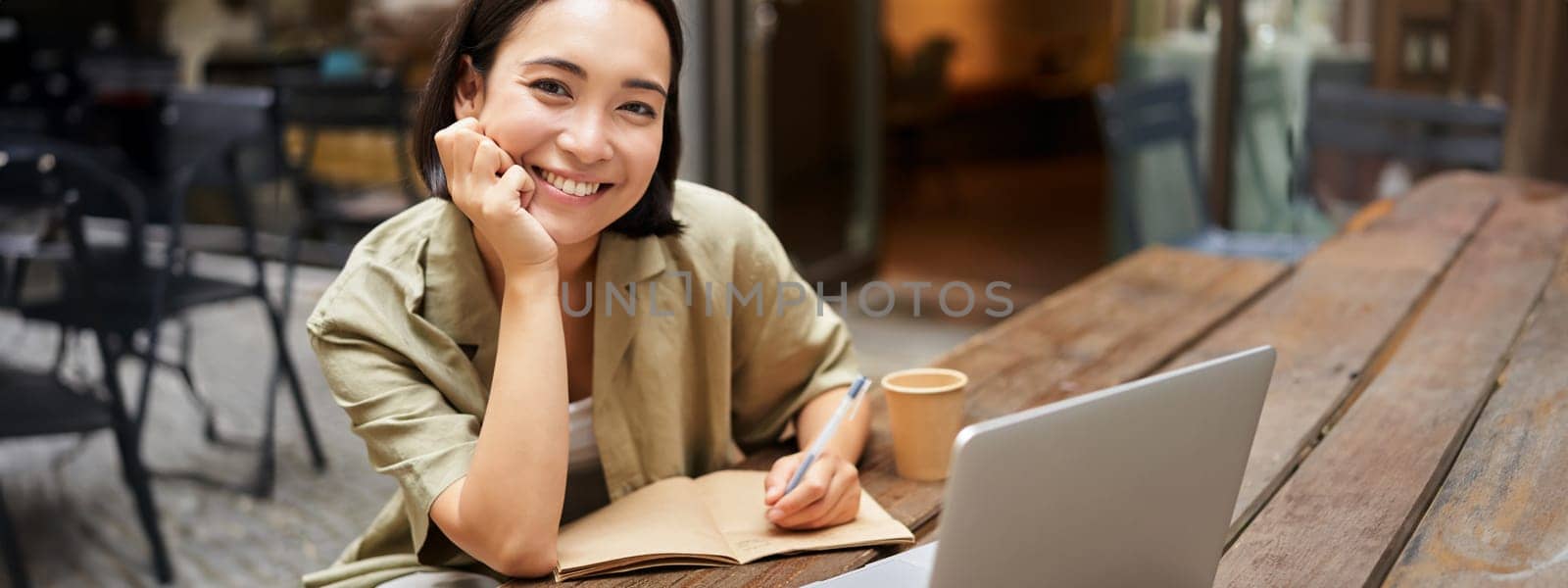 Portrait of young korean girl making notes, listening online meeting, lecture, looking at laptop screen, working remotely from cafe.