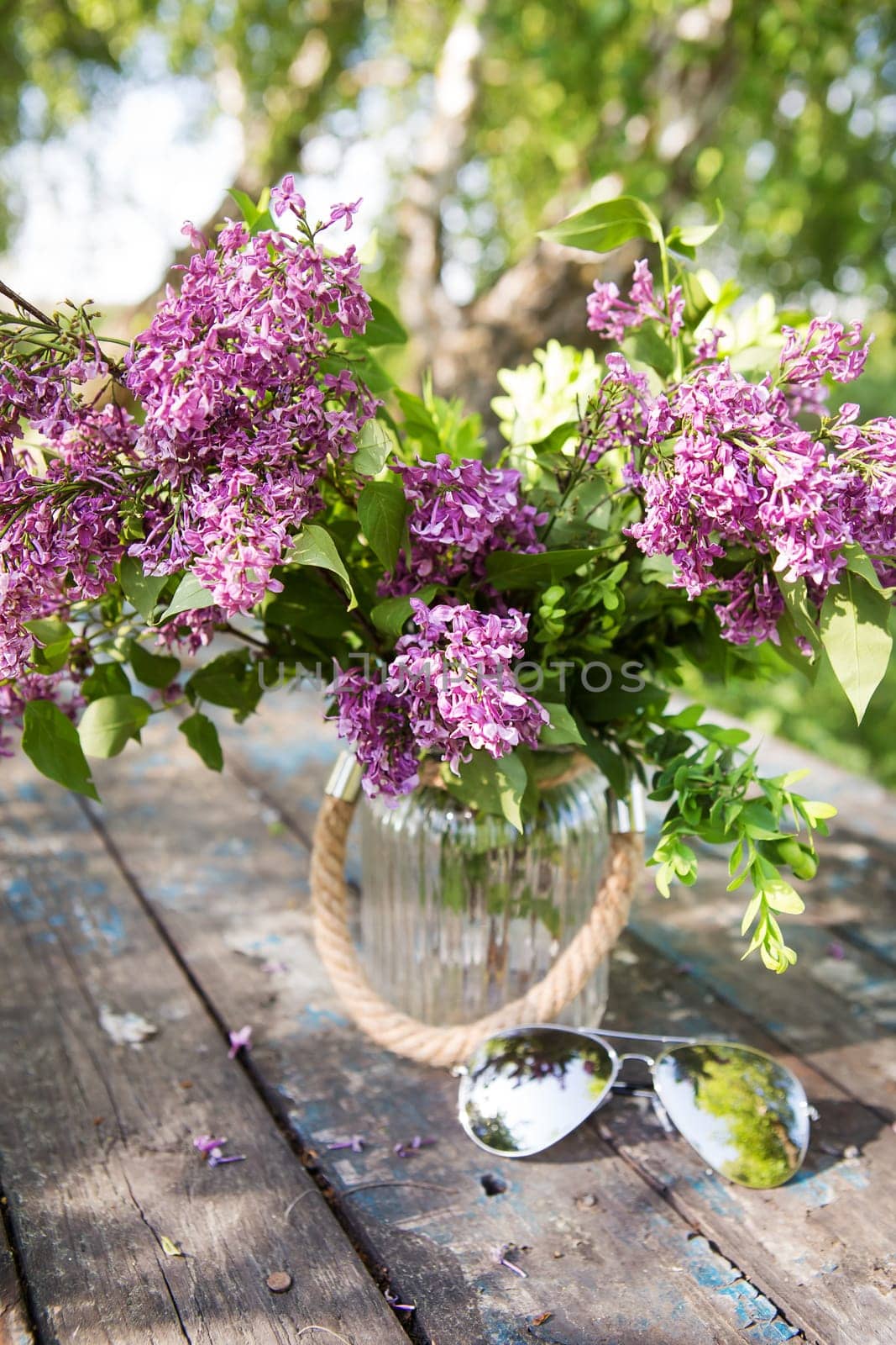 sunglasses and a beautiful bouquet of lilacs on an old table.