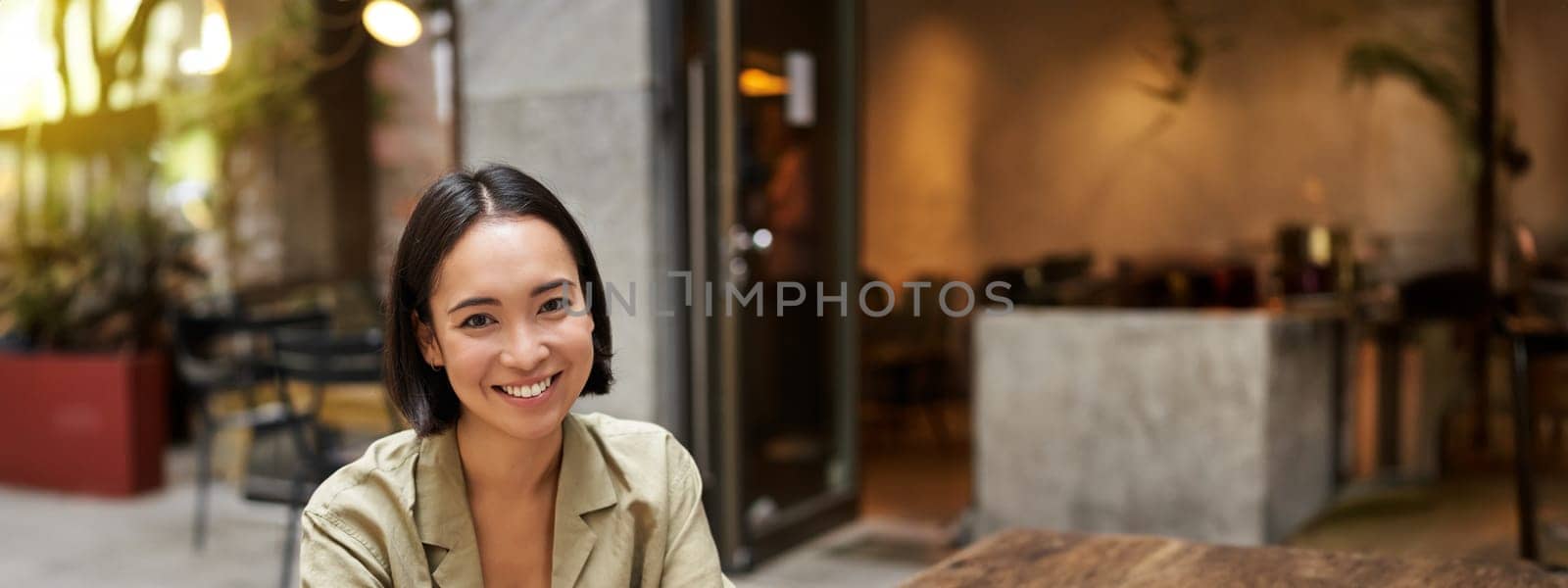 Young digital nomad, woman working remotely from cafe, typing on laptop, sitting outside and smiling.