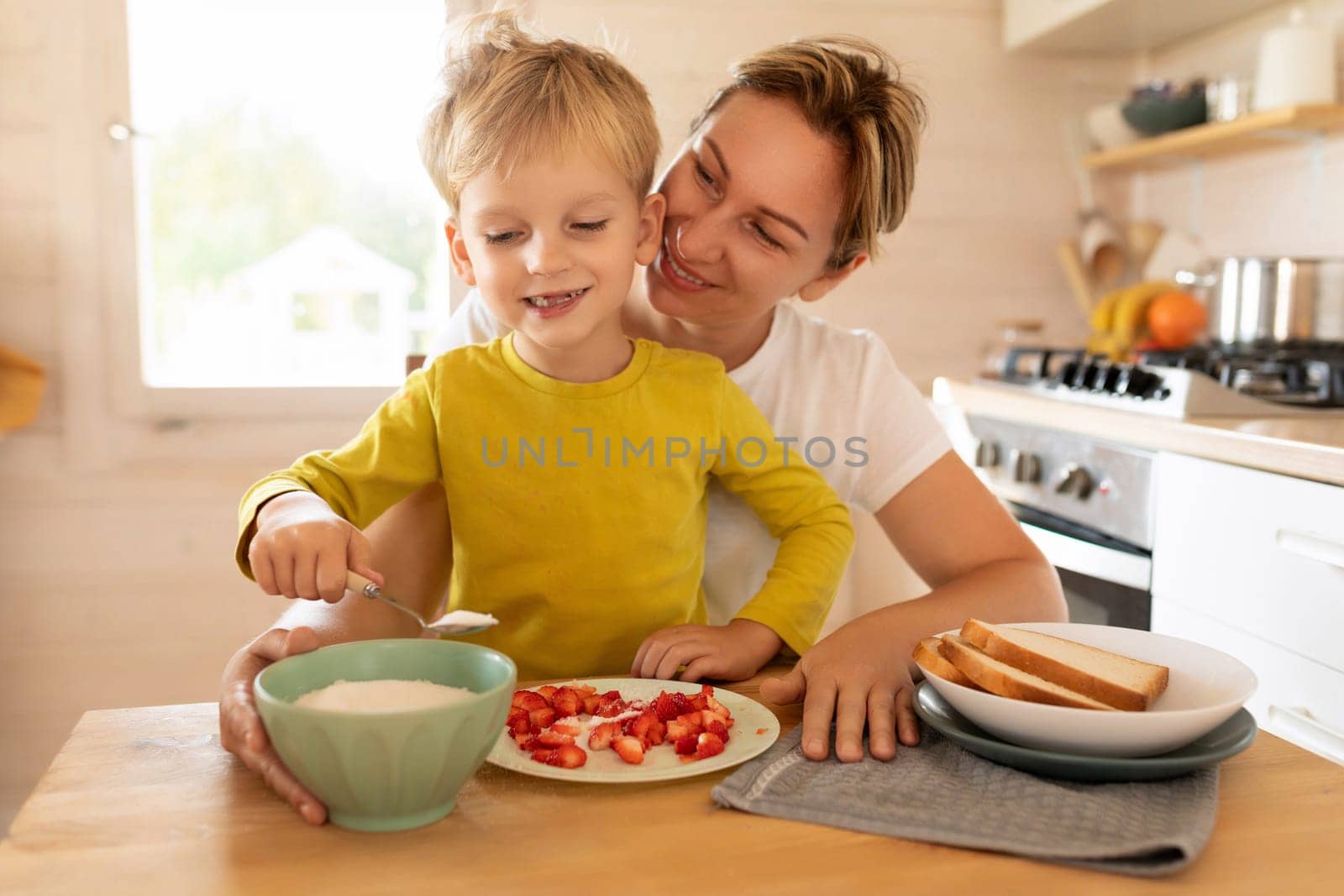 lifestyle concept, young mother and son sitting at the table in the kitchen with plates of food by TRMK