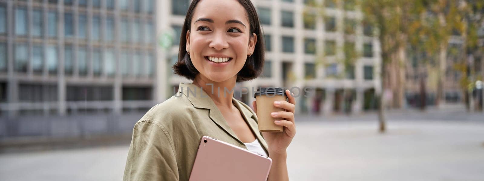 Portrait of asian girl with tablet, drinks coffee on street, walking in city centre.