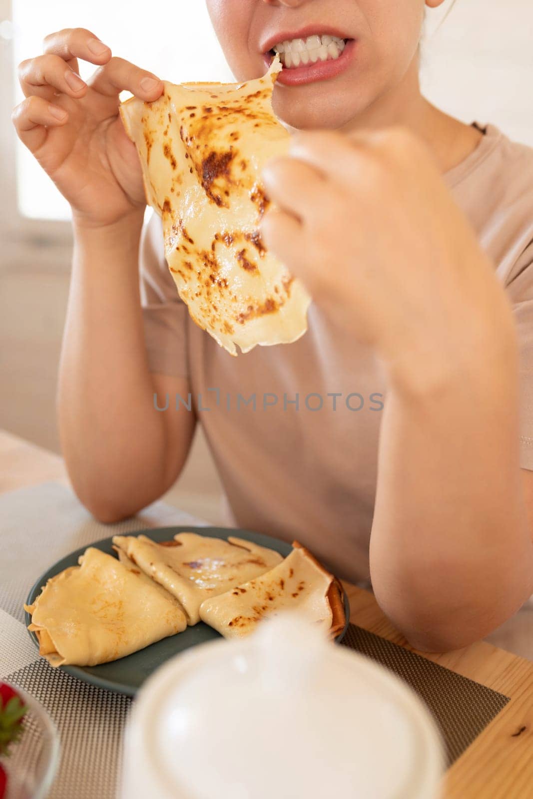 a young woman pulls a piece of pancake into her mouth. concept of gluttony and eating disorder.