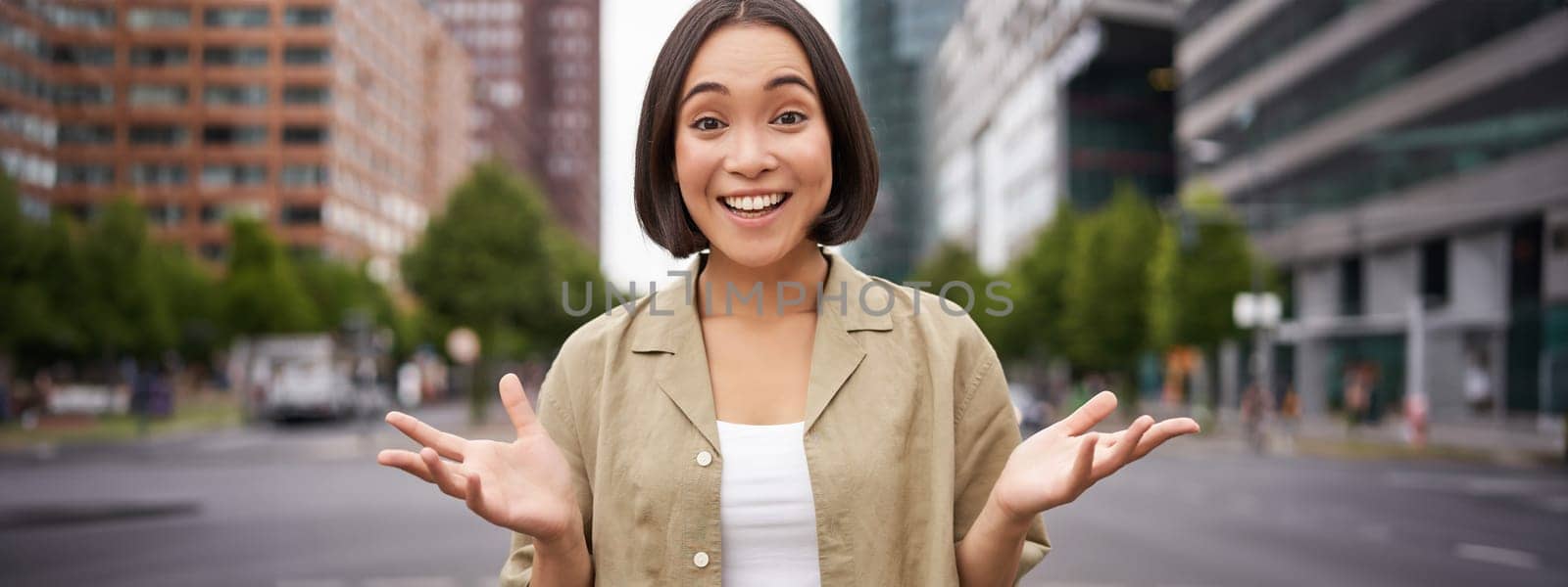 Modern asian girl standing on street with surprised face, looking impressed and amazed, hear awesome news.