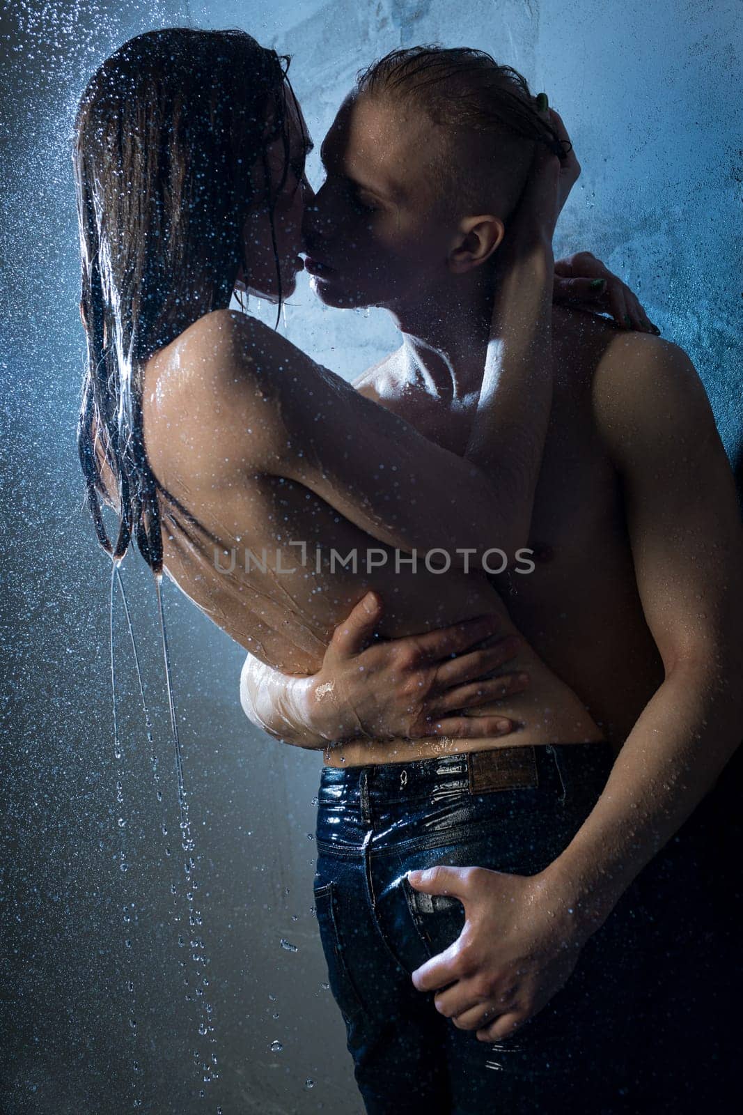 Girl wearing only jeans kissing with a nude man in a shower in the dark