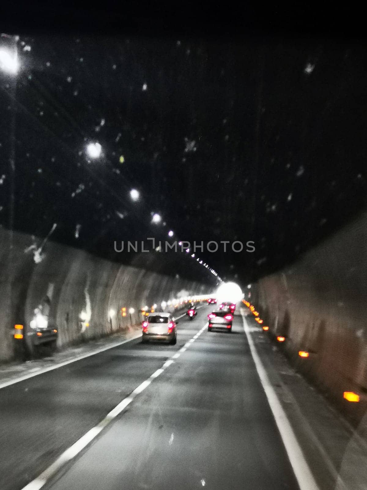 Vehicles navigate through a dark tunnel, lit by bright overhead lights, creating a clear path as they approach the exit. The ambiance is serene and modern.