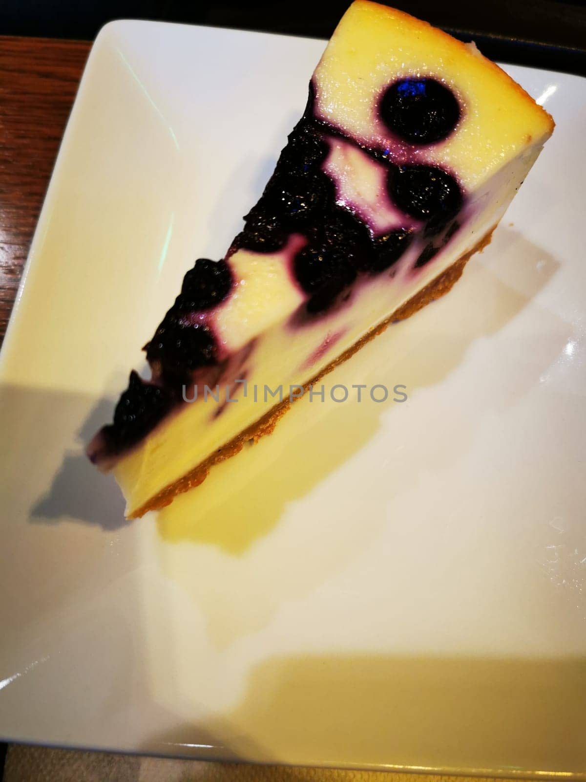 Blueberry cheesecake, featuring a creamy topping and crumbly crust, is elegantly presented on a white plate at a café, inviting patrons to enjoy a sweet treat.