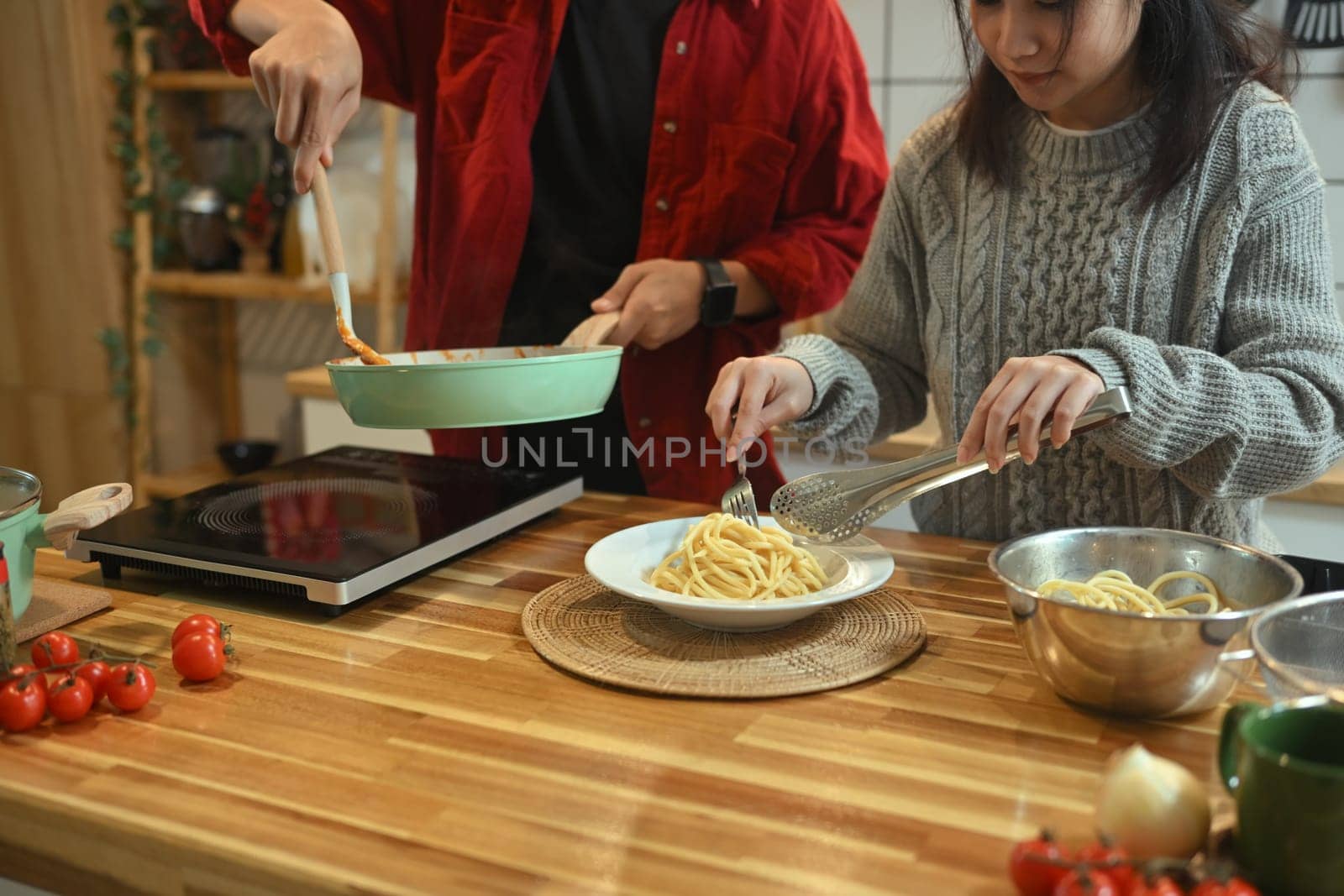 Happy couple preparing a delicious pasta dish for festive dinner.