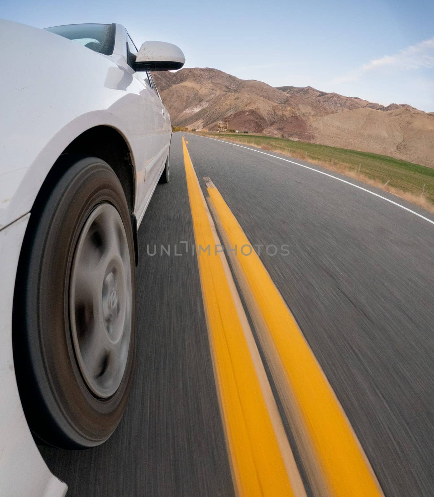 A car is driving down a road with yellow lines. The car is white and is in the middle of the road