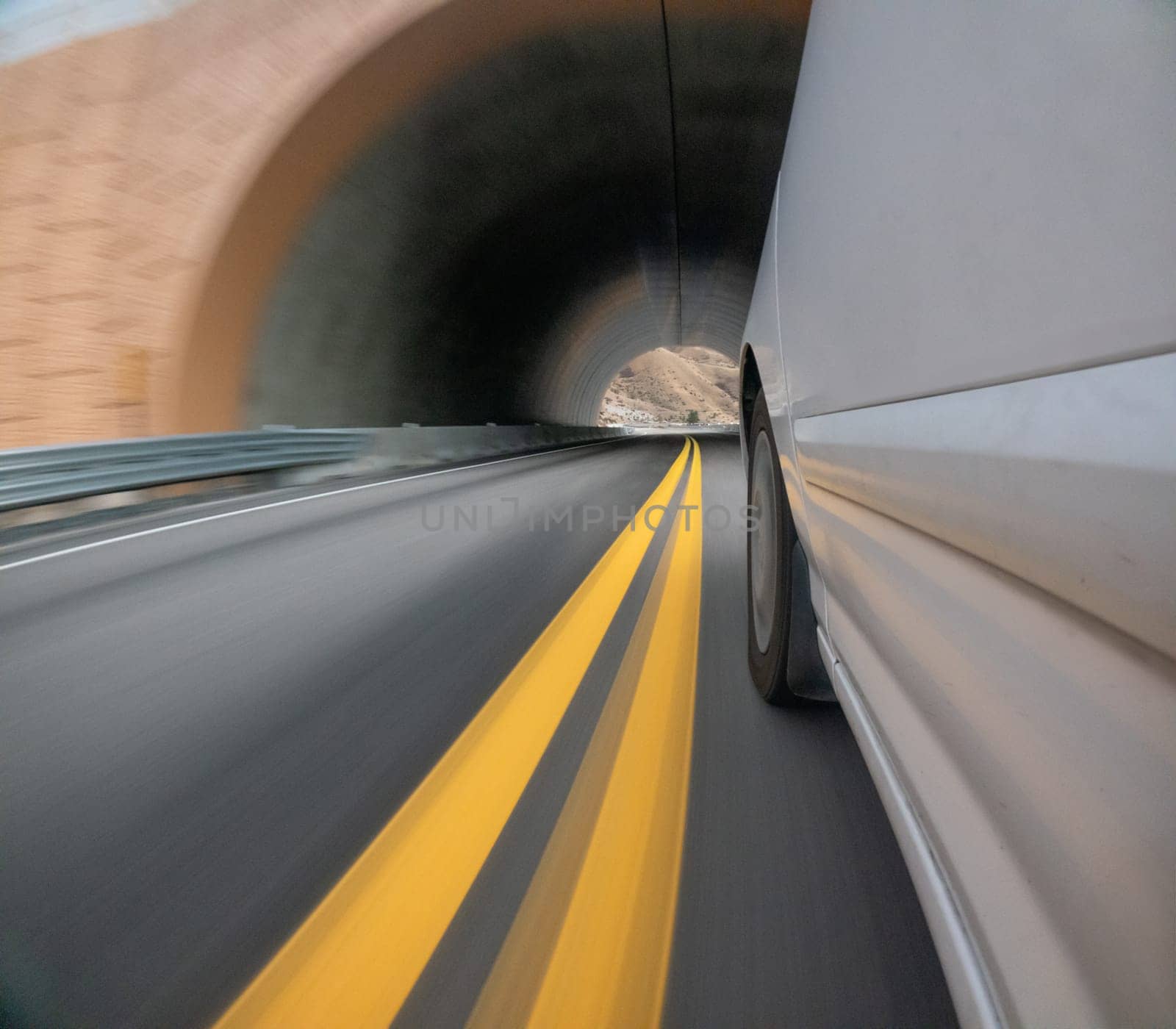 A car is driving down a road with yellow lines. The car is white and is in the middle of the road