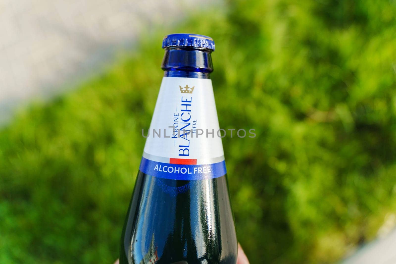 Tyumen, Russia-August 10, 2024: hand grasps a chilled bottle of alcohol-free Krone Blanche while sitting on a swing in a sunny park