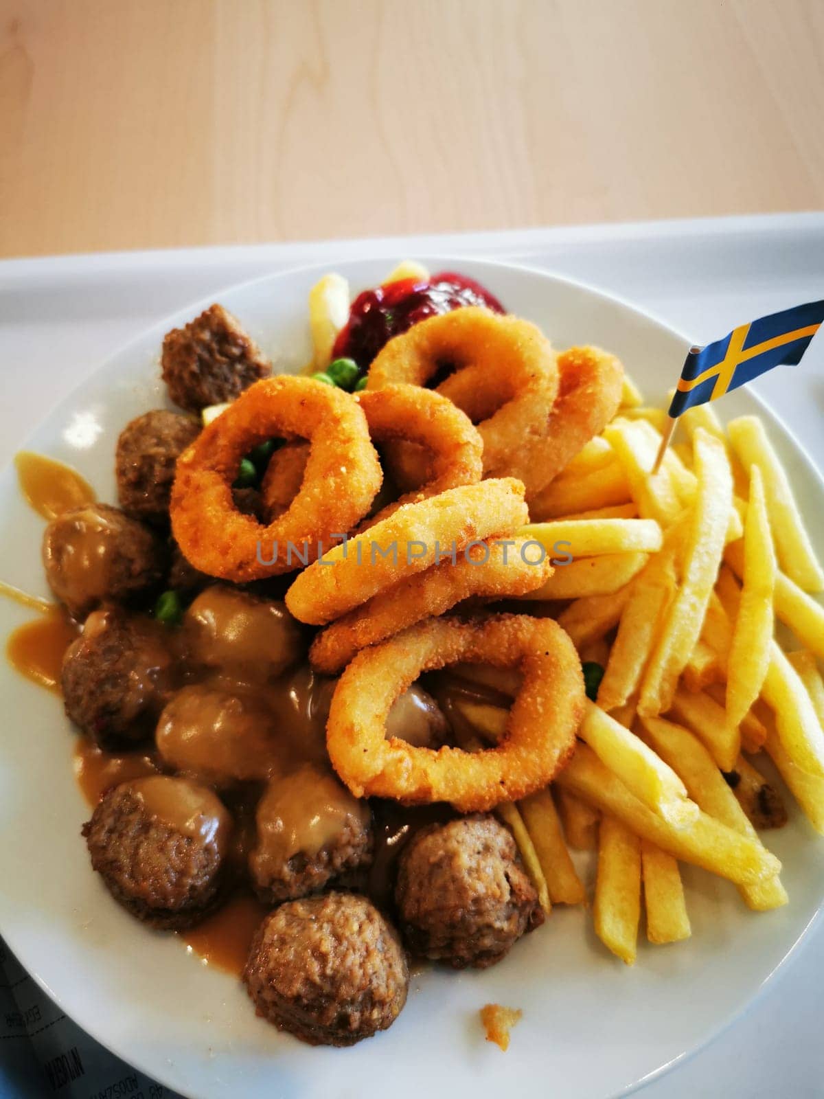 This hearty meal features Swedish meatballs drenched in gravy, accompanied by crispy onion rings, golden fries, and a touch of ketchup, perfect for a satisfying lunch.
