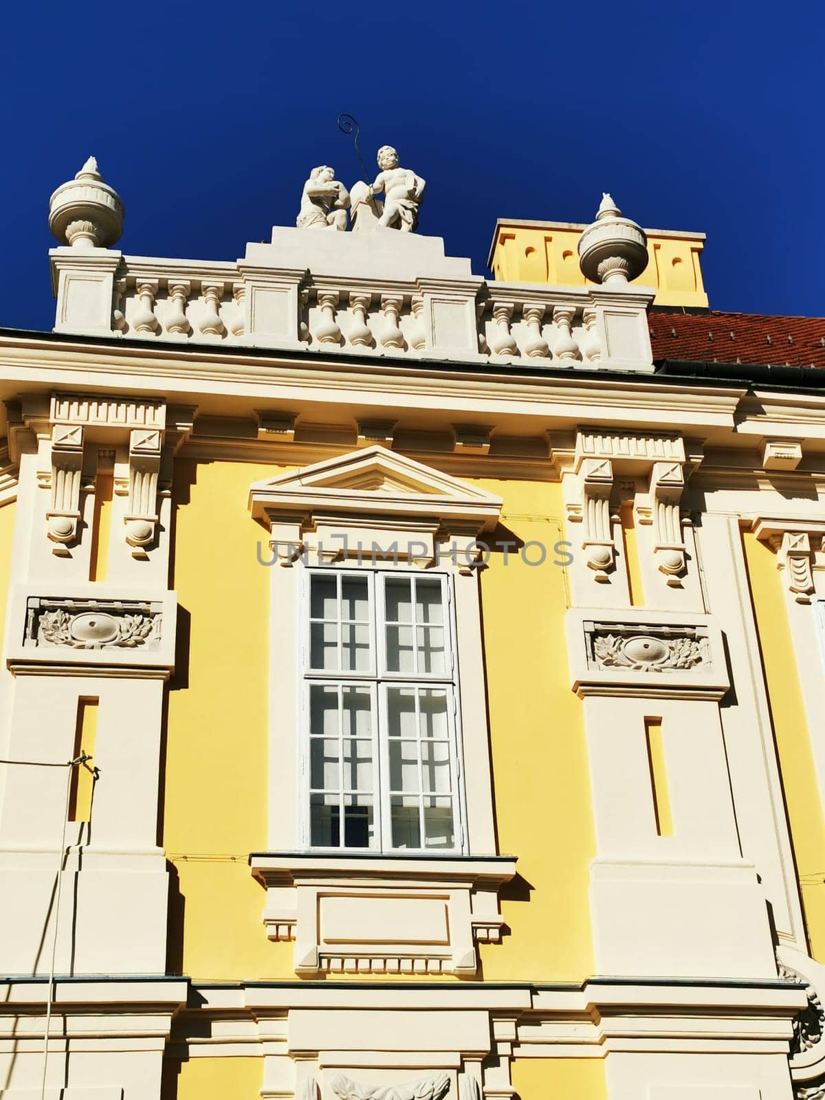 The vibrant yellow facade of a beautifully detailed building features exquisite architectural elements, highlighting the artistry of historical European design against a clear blue sky.