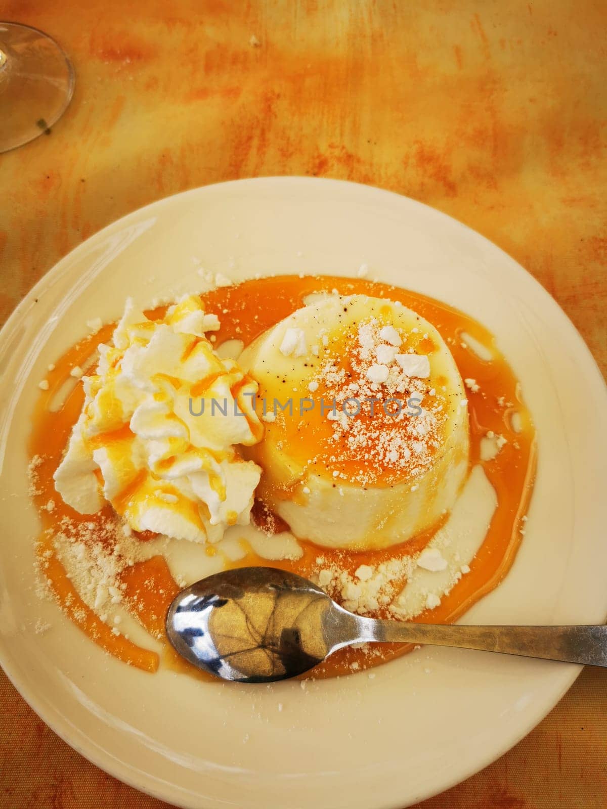 A creamy dessert sits on a plate, drizzled with caramel sauce and surrounded by a dollop of whipped cream and powdered sugar, inviting sweet indulgence.