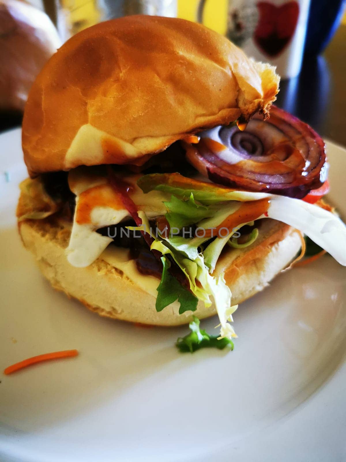 A freshly made burger stacked with lettuce, onion, and tomato sits on a white plate, showcasing its vibrant, appetizing ingredients at a casual diner.