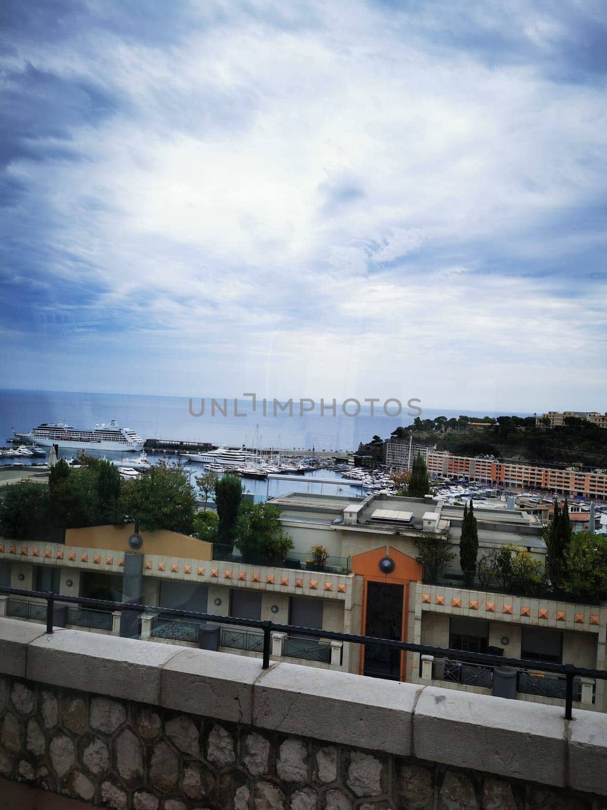 The backdrop features a busy harbor dotted with luxurious yachts as clouds partially obscure the sun, showcasing the vibrant coastline of Monaco.