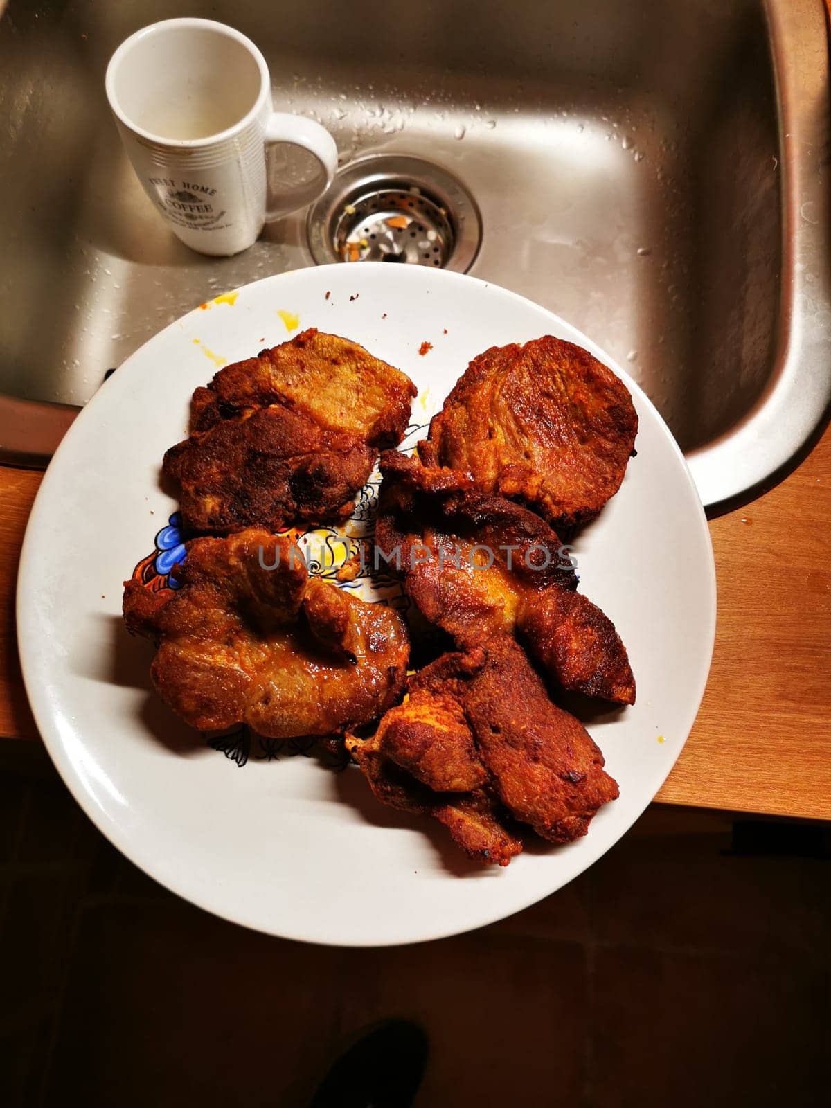 A delicious assortment of crispy fried chicken pieces is arranged on a decorative plate, contrasting with the nearby kitchen sink and mug, creating a warm homey atmosphere.
