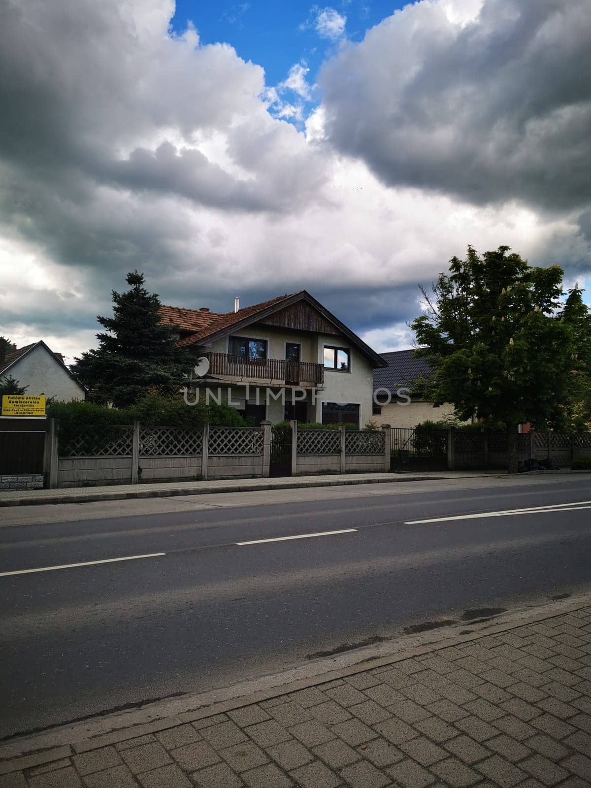 A peaceful suburban house stands amidst cloudy skies, with green trees lining the road. The evening light casts a calm ambiance to the setting.