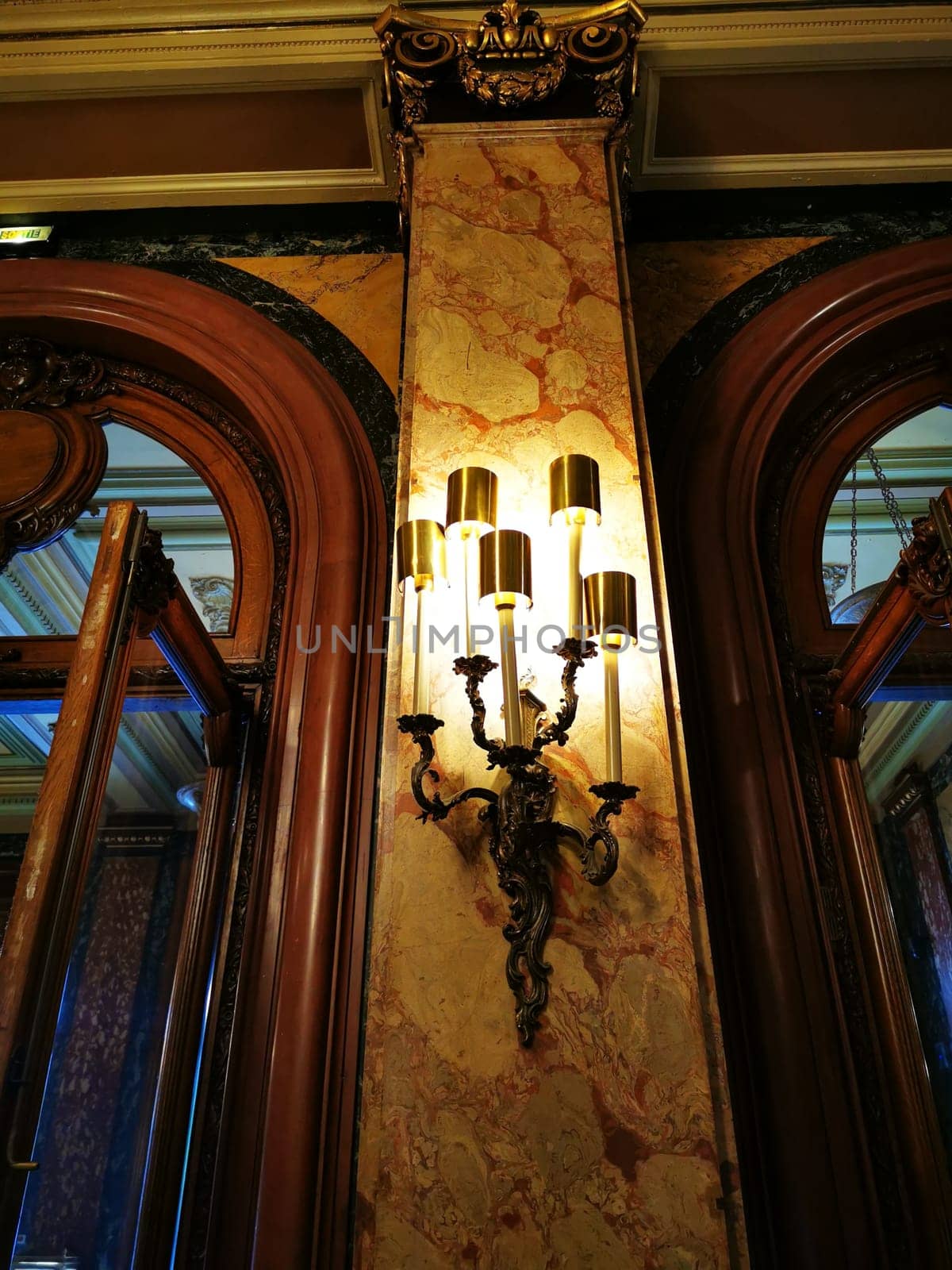 A vintage wall sconce casts a warm glow on the intricately detailed marble wall of a historic building, showcasing classic architecture and rich decor.
