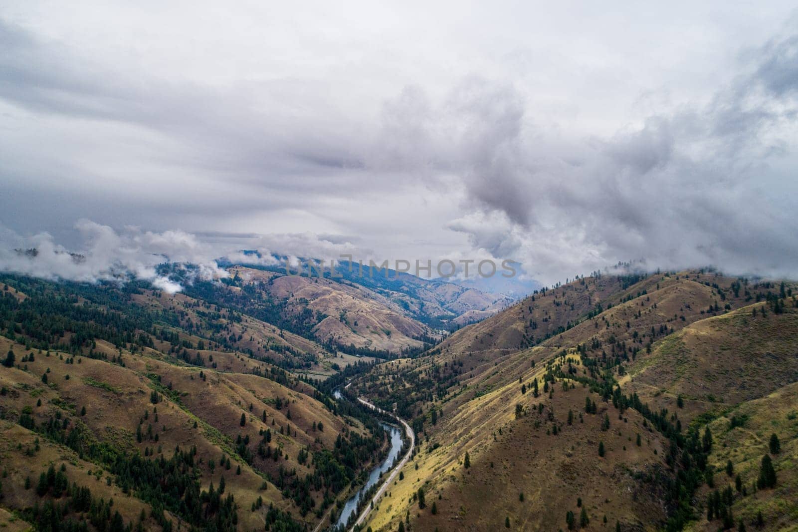 The sky is cloudy and the mountains are covered in trees. The landscape is beautiful and peaceful. The clouds give the scene a sense of calmness and serenity