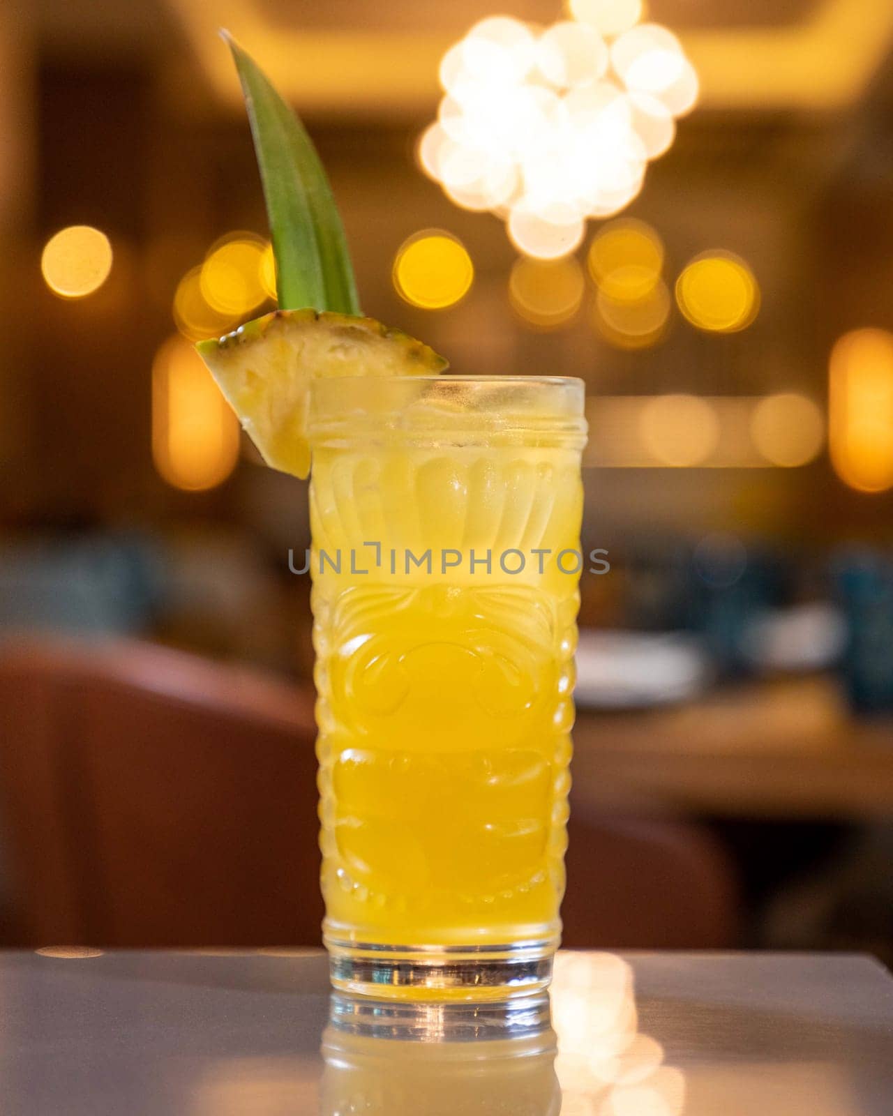 Refreshing pineapple cocktail served in tiki-style glass standing on bar with blurred restaurant background