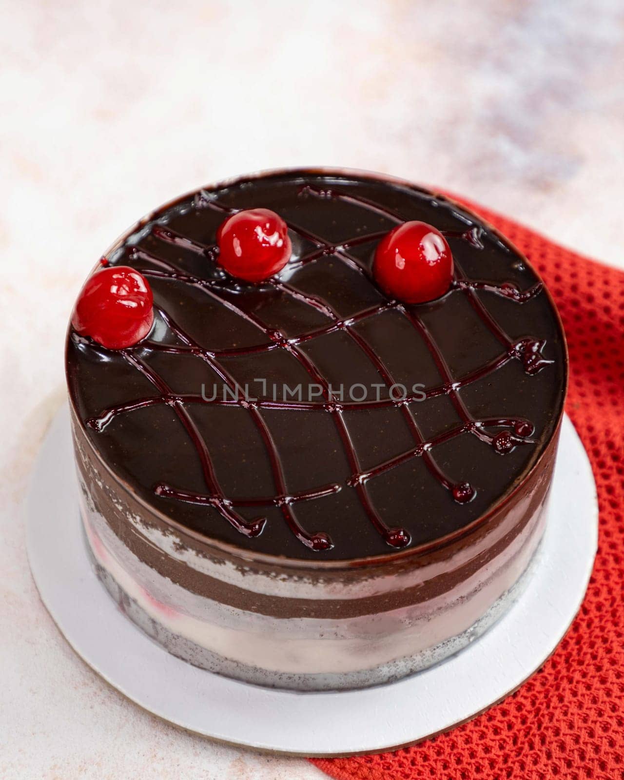 Chocolate cake with cherries covered with chocolate glaze standing on white plate on red knitted fabric