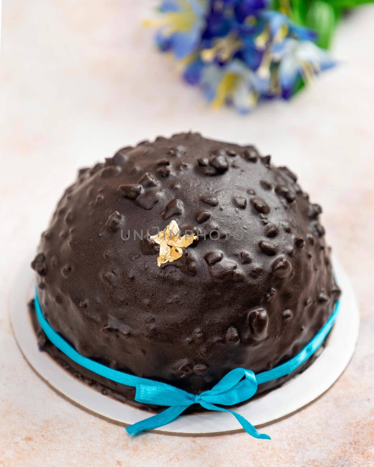 Chocolate bomb cake with a blue ribbon decorated with a gold leaf on a marble table