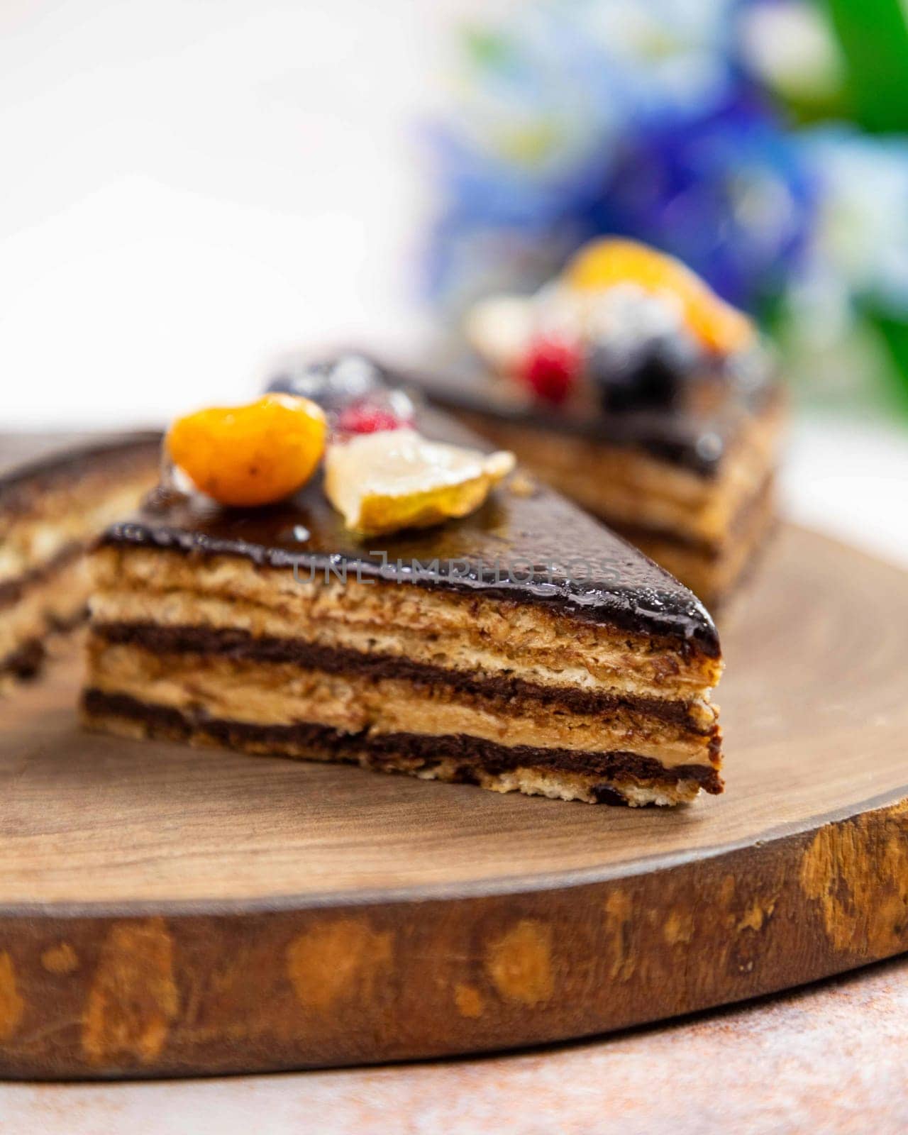 Slice of delicious cake with chocolate and fruits topping is sitting on a wooden board